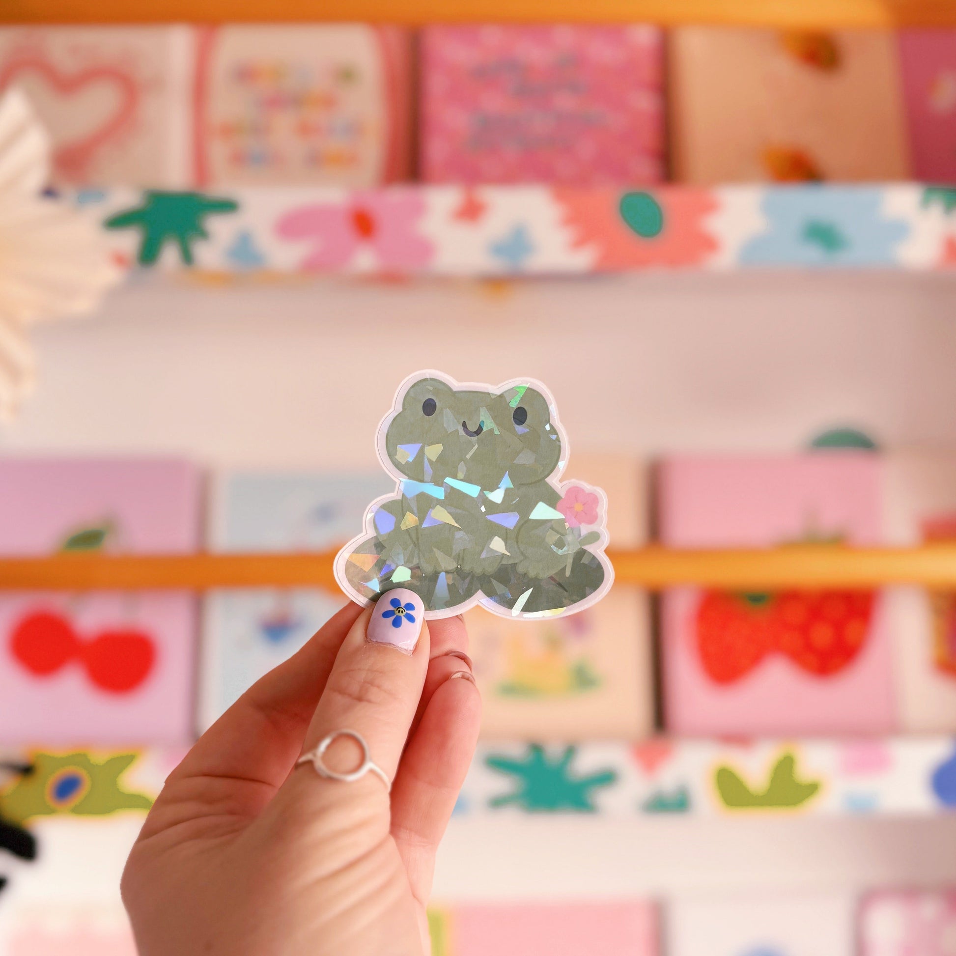 A holographic sticker featuring a frog sat on a lily pad.
