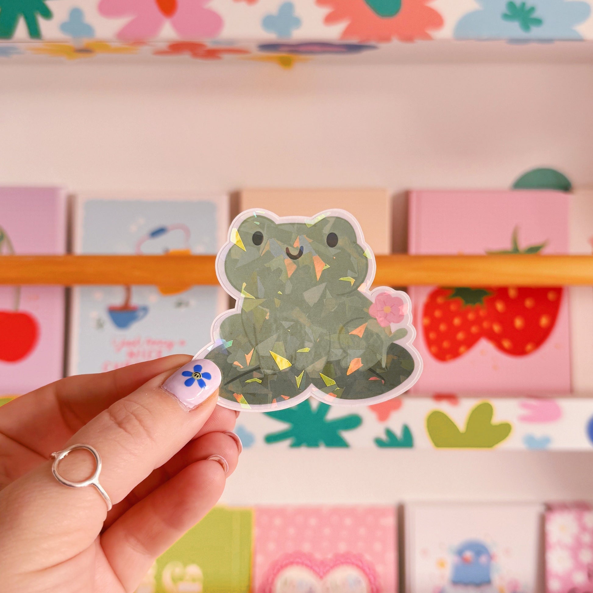 A holographic sticker featuring a frog sat on a lily pad.