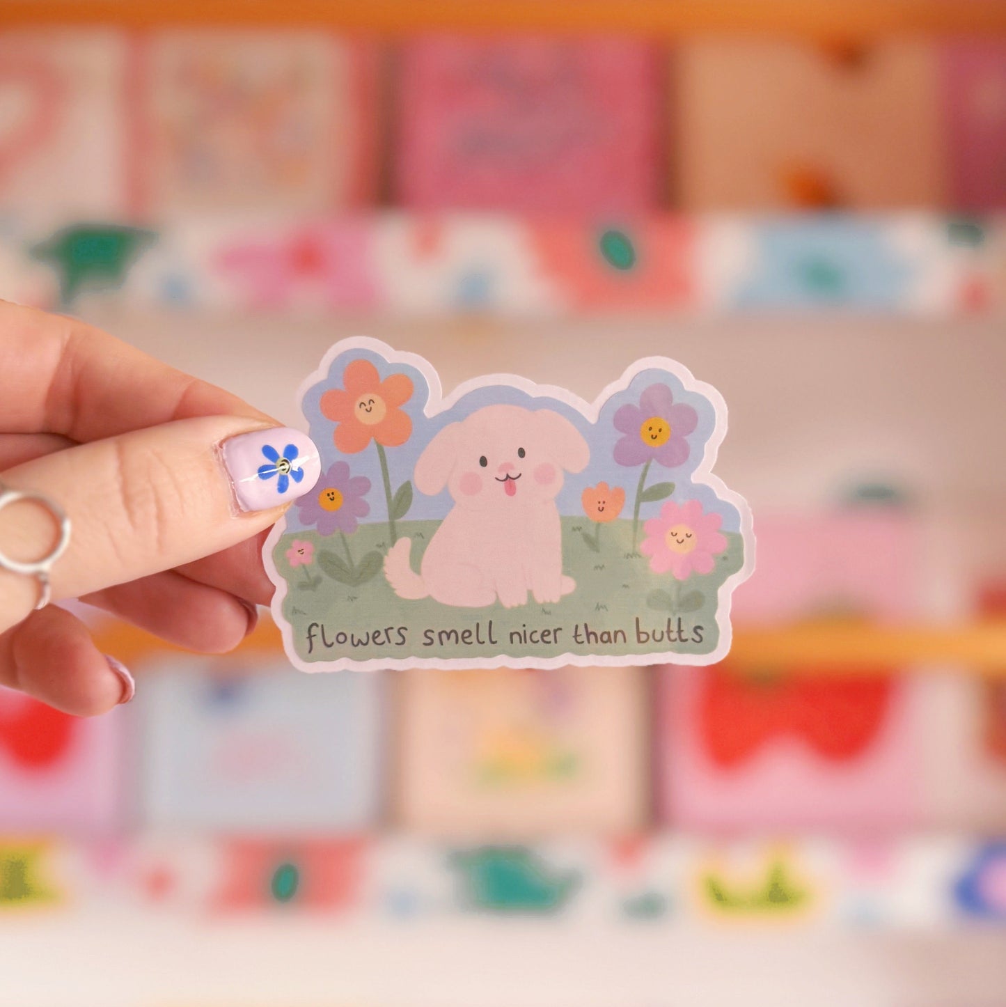 An illustrated sticker of a dog sat amongst flowers, with the quote 'flowers smell nicer than butts' underneath'.