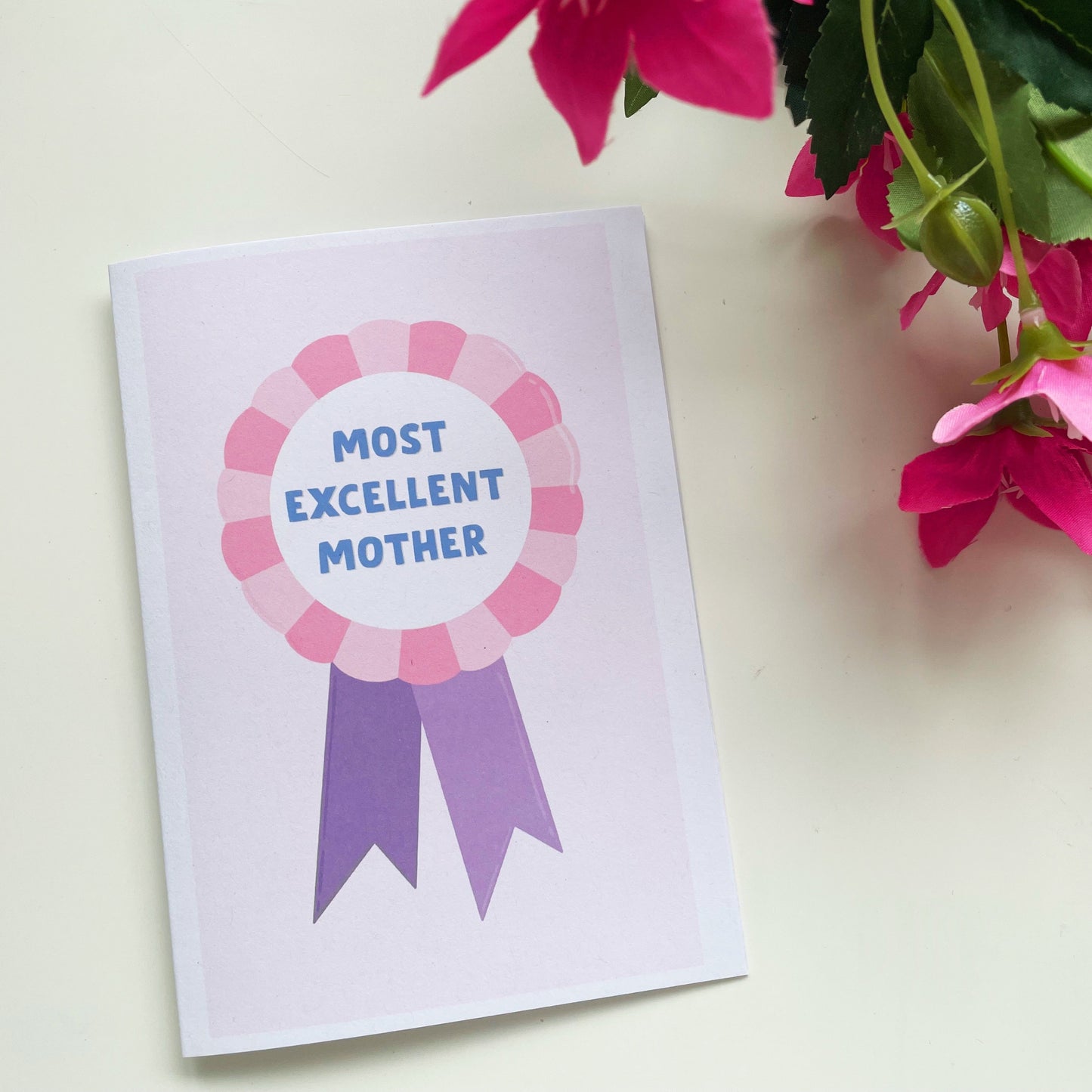 A Mother's Day card, with a pink and purple rosette and the words 'Most Excellent Mother' written on the rosette.