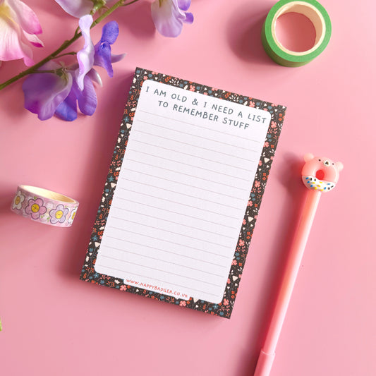 Notepad with decorative border, pen, and tape on a pink background