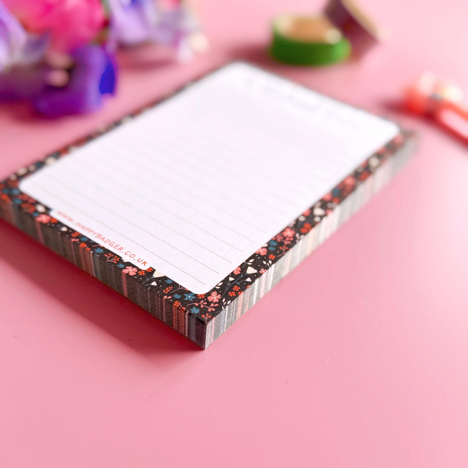 Floral-patterned notepad on a pink surface with colorful flowers in the background