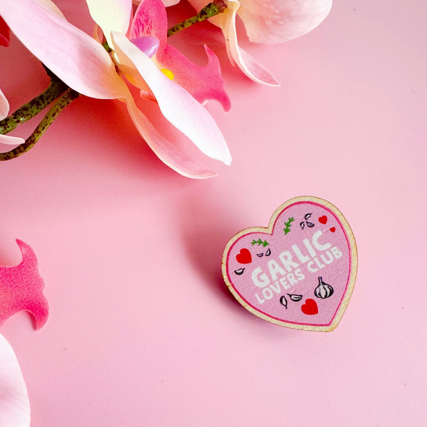 A wooden eco friendly pin badge of a pink heart with the words garlic lovers club inside of it.