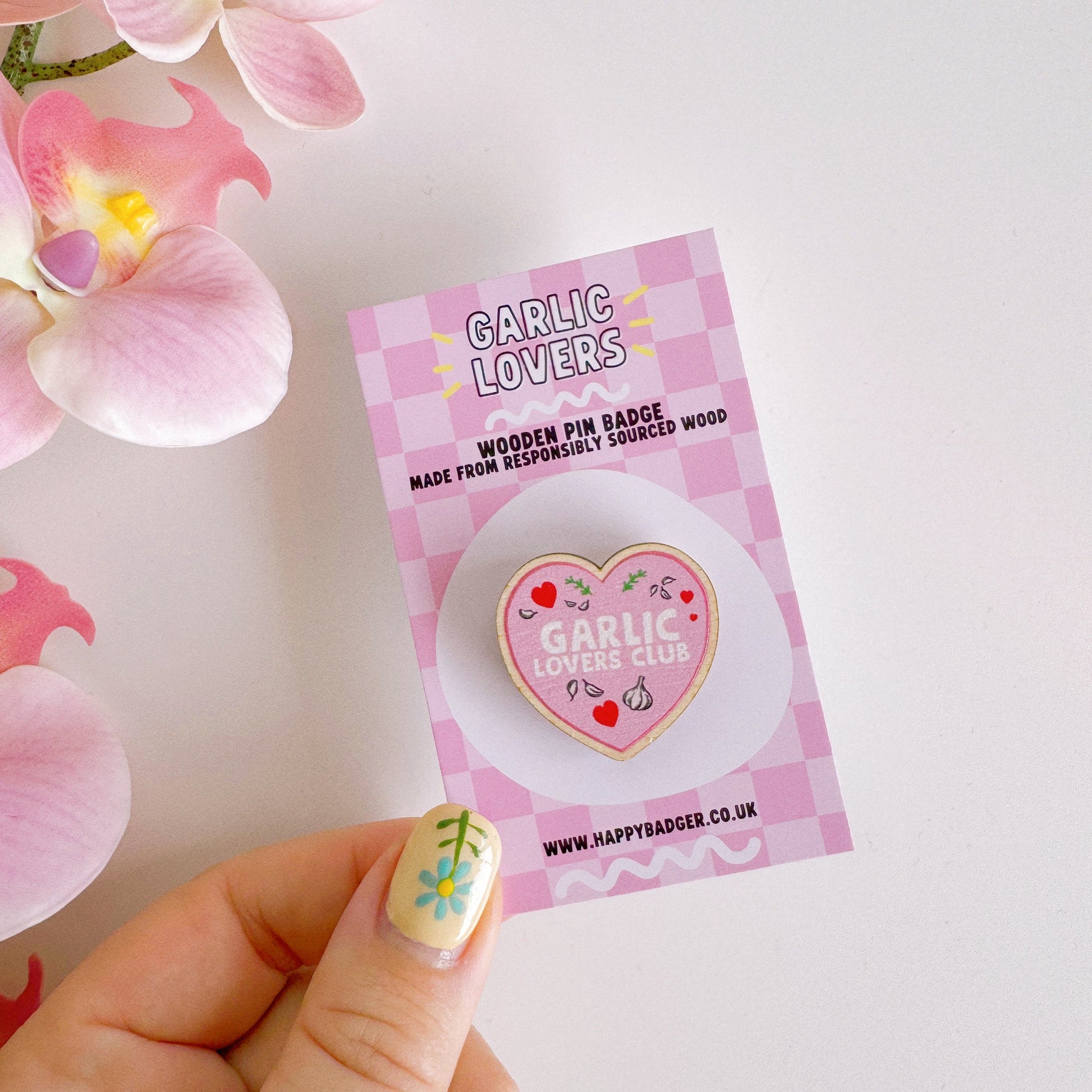 A pink heart shaped wooden pin badge, with the words 'garlic lovers club' on the front