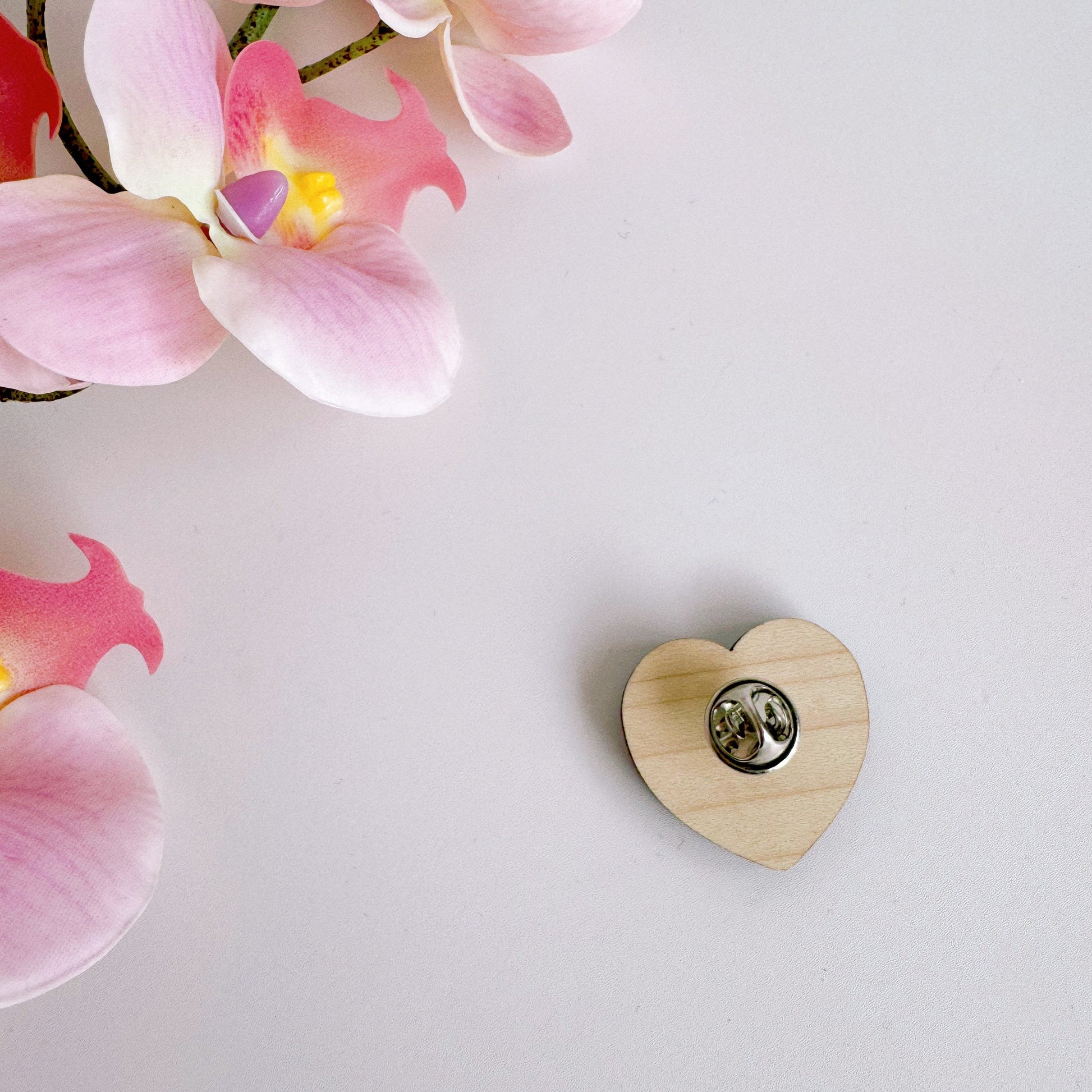 A pink heart shaped wooden pin badge, with the words 'garlic lovers club' on the front