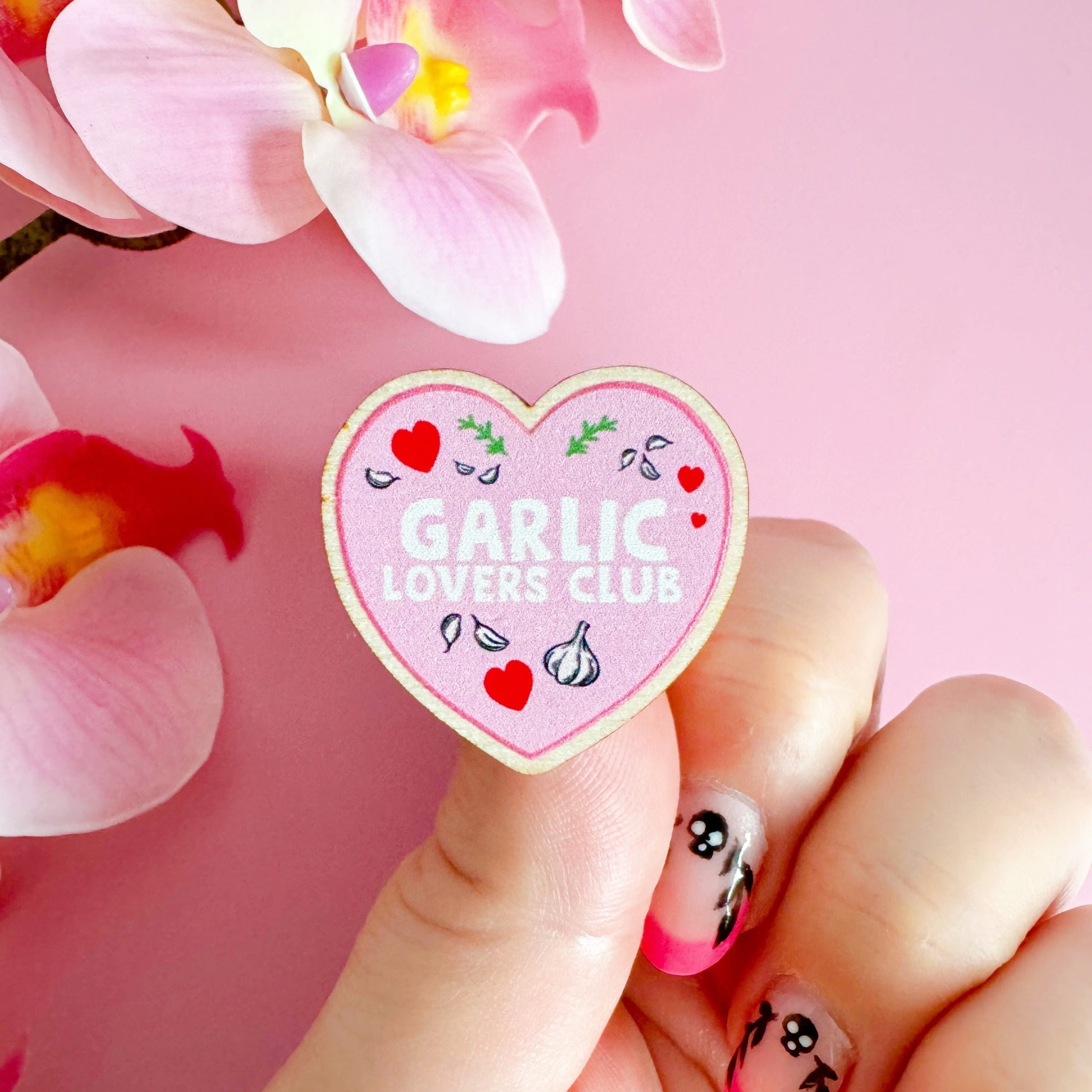 A wooden eco friendly pin badge of a pink heart with the words garlic lovers club inside of it.