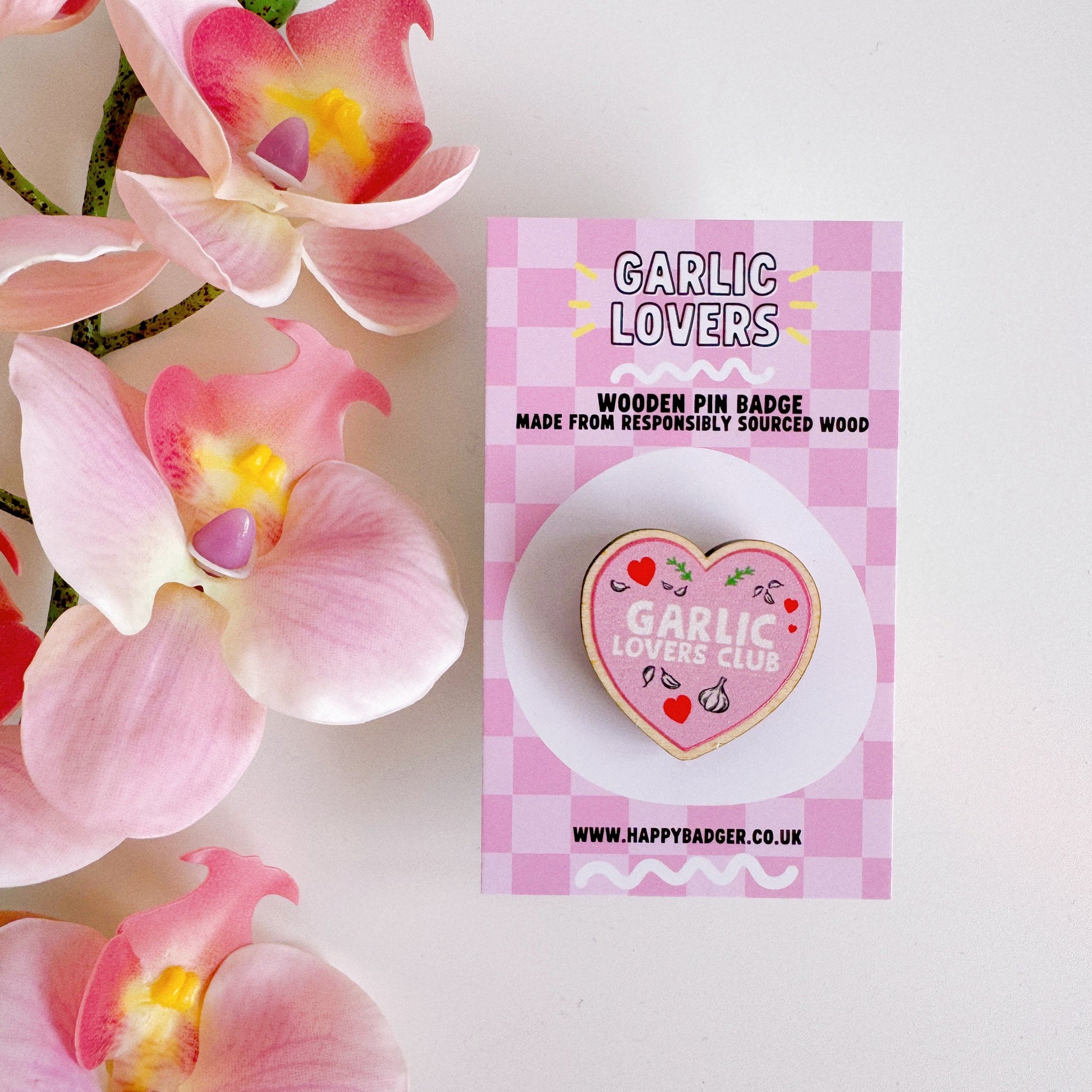A pink heart shaped wooden pin badge, with the words 'garlic lovers club' on the front