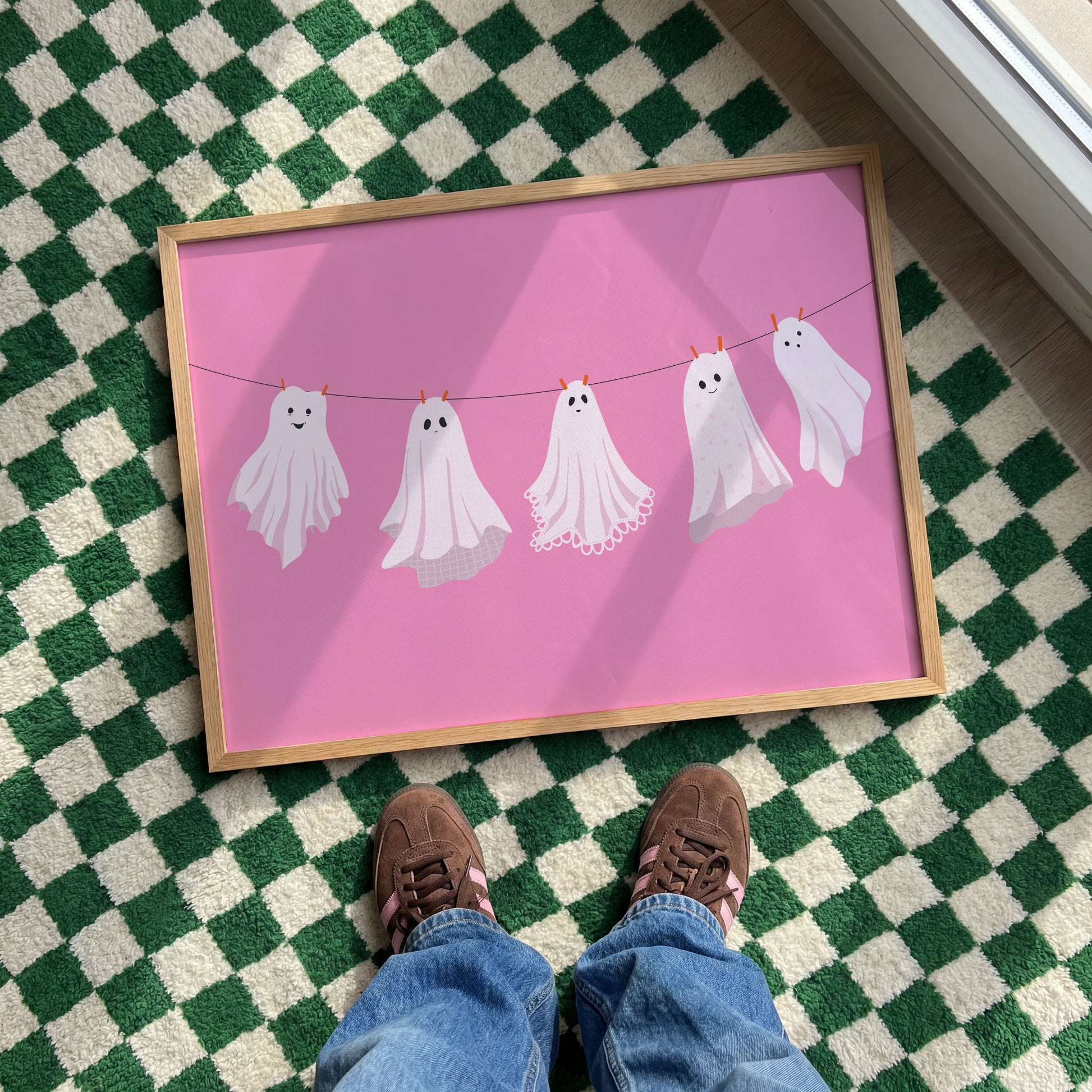 A pink Halloween print with five different ghosts made from bedsheets, hanging on a washing line.