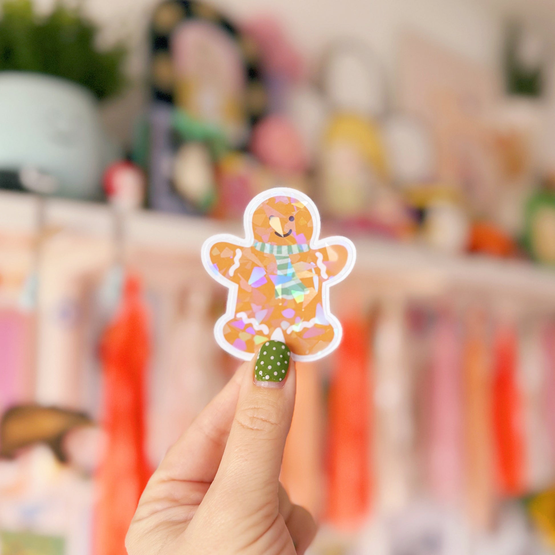 Hand holding a colorful sticker of a gingerbread man against a blurred indoor background
