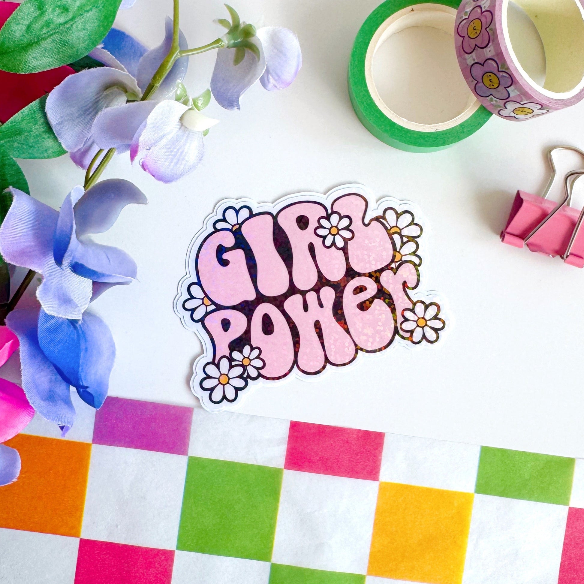 A holographic sticker with the words 'GIRL POWER' in bold pink lettering, with little white daisies surrounding the text.