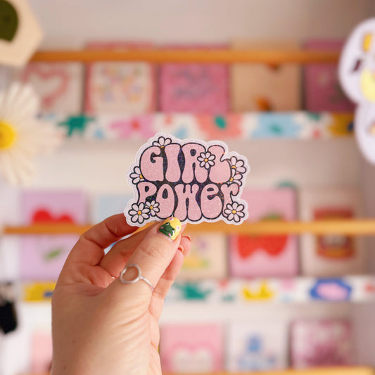 Hand holding a 'Girl Power' sticker in front of a colourful display