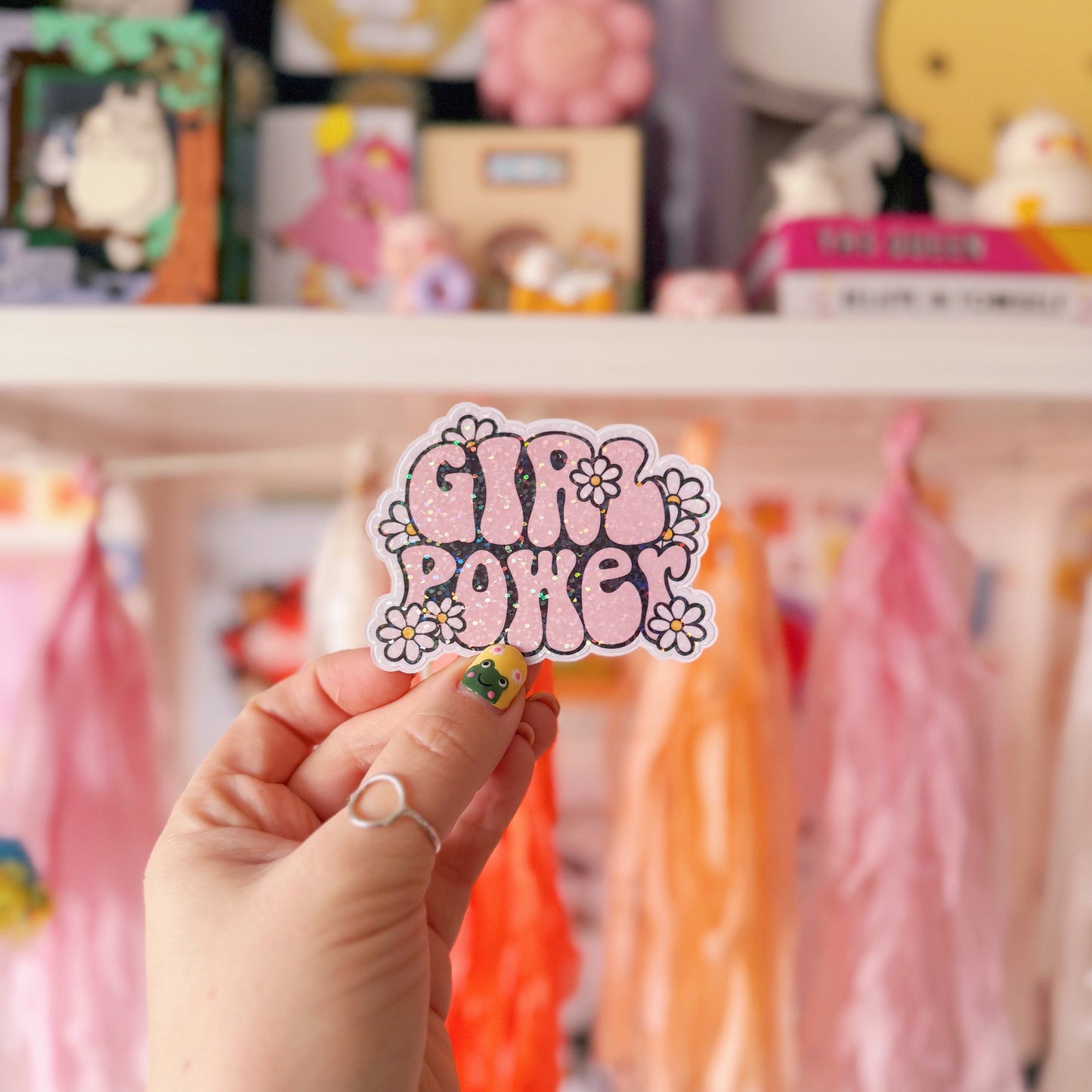 Hand holding a 'Girl Power' sticker in front of a colourful display
