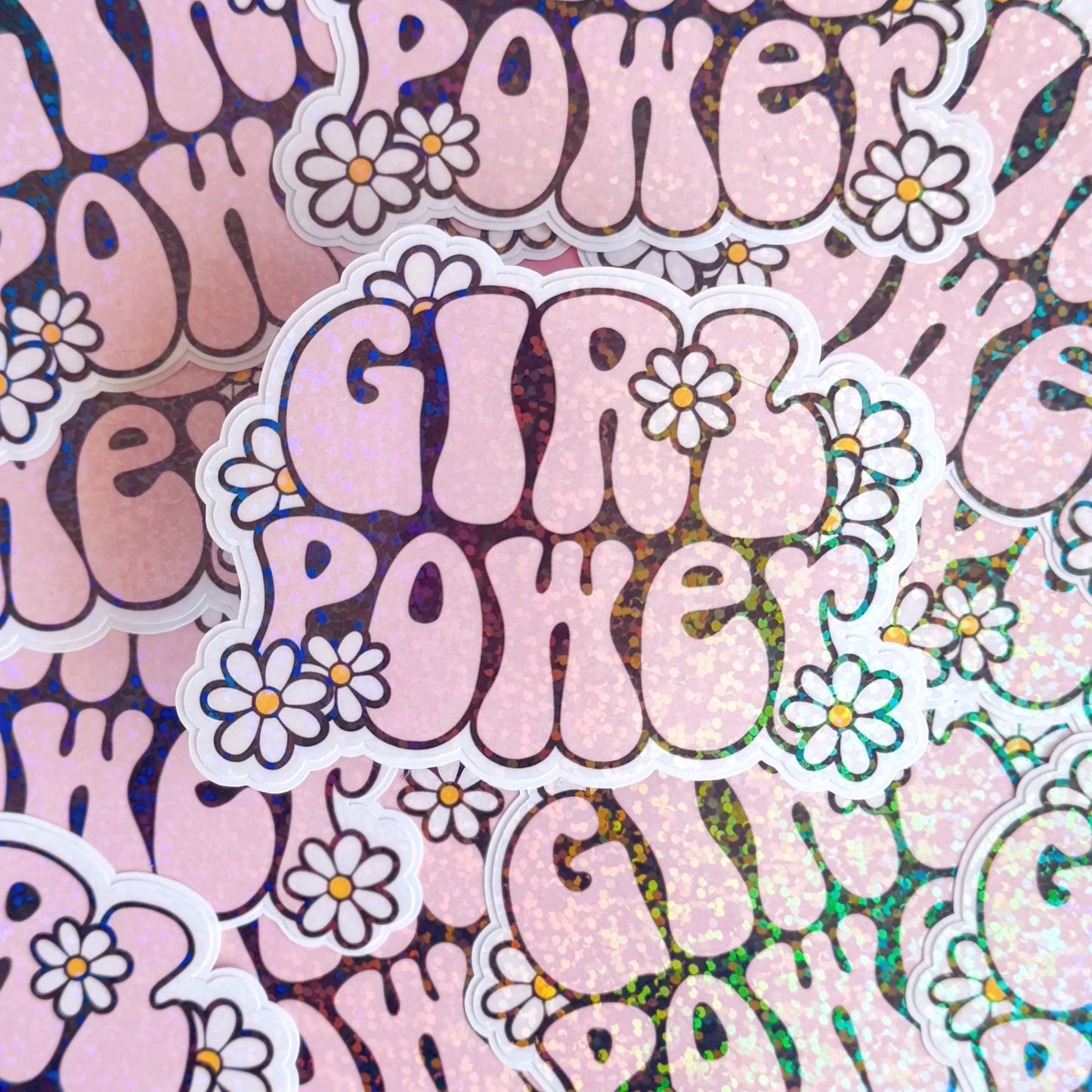 A holographic sticker with the words 'GIRL POWER' in bold pink lettering, with little white daisies surrounding the text.