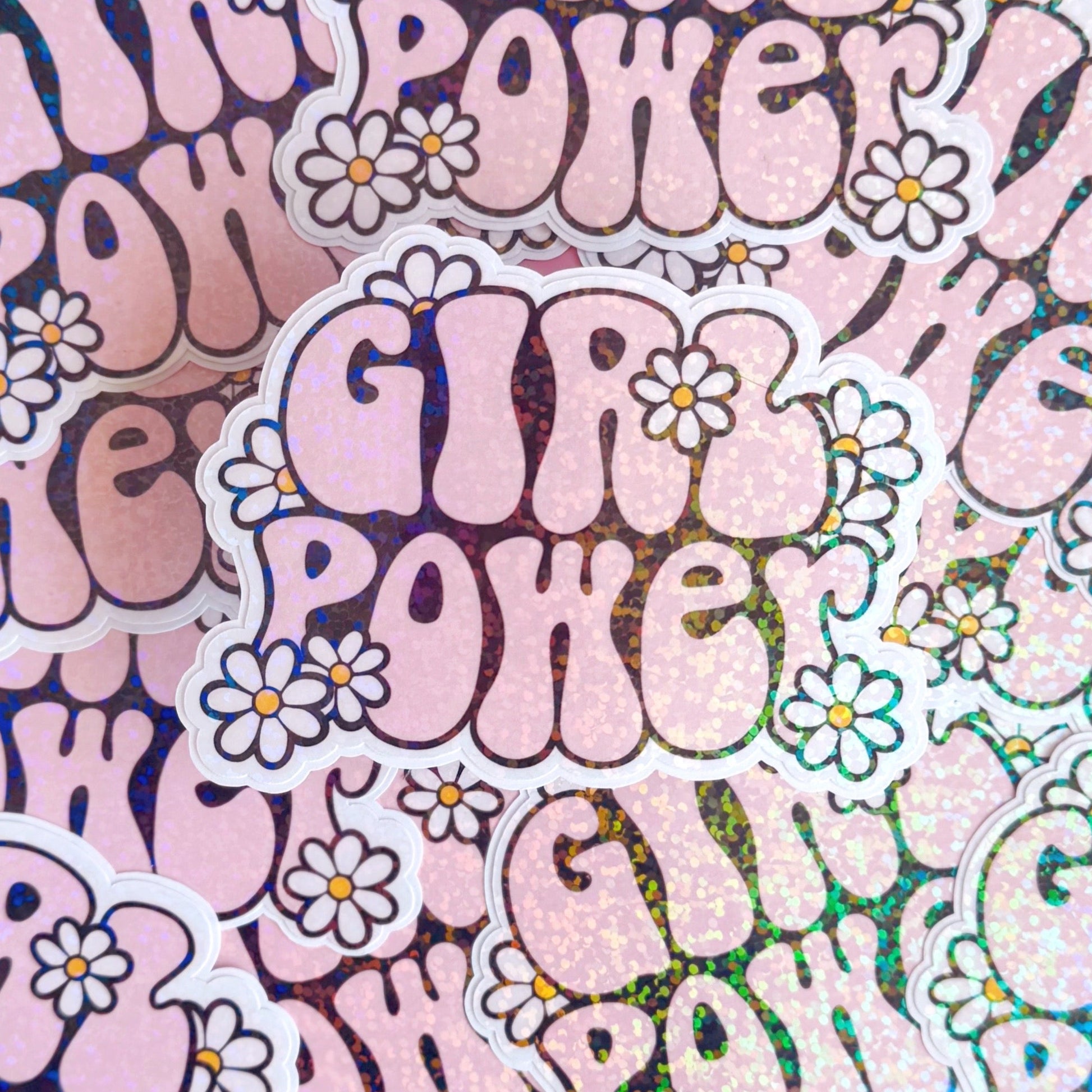 A holographic sticker with the words 'GIRL POWER' in bold pink lettering, with little white daisies surrounding the text.