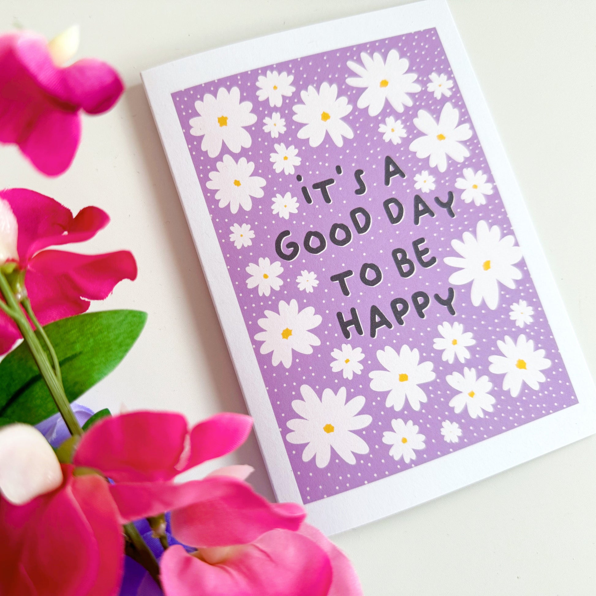 A purple card, with daisies, and the message 'it's a good day to be happy' in the centre. 