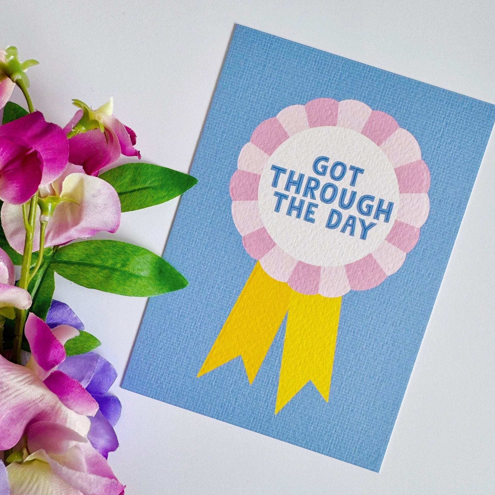 A blue postcard, with a rosette in pink and yellow, saying got through the day.