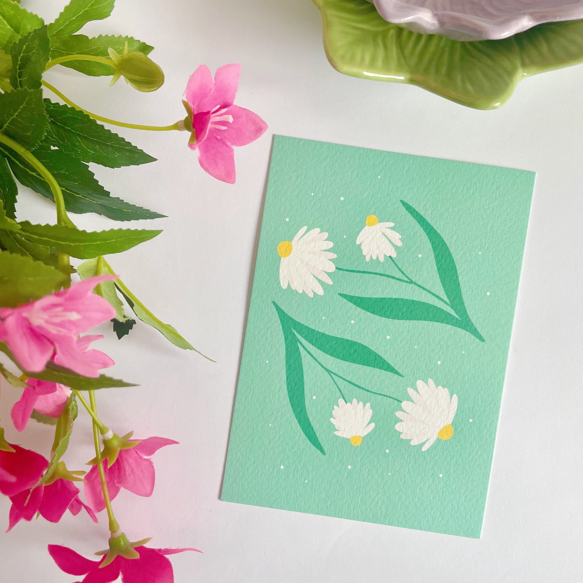 A textured postcard, with two illustrations of daisy stems on the front.