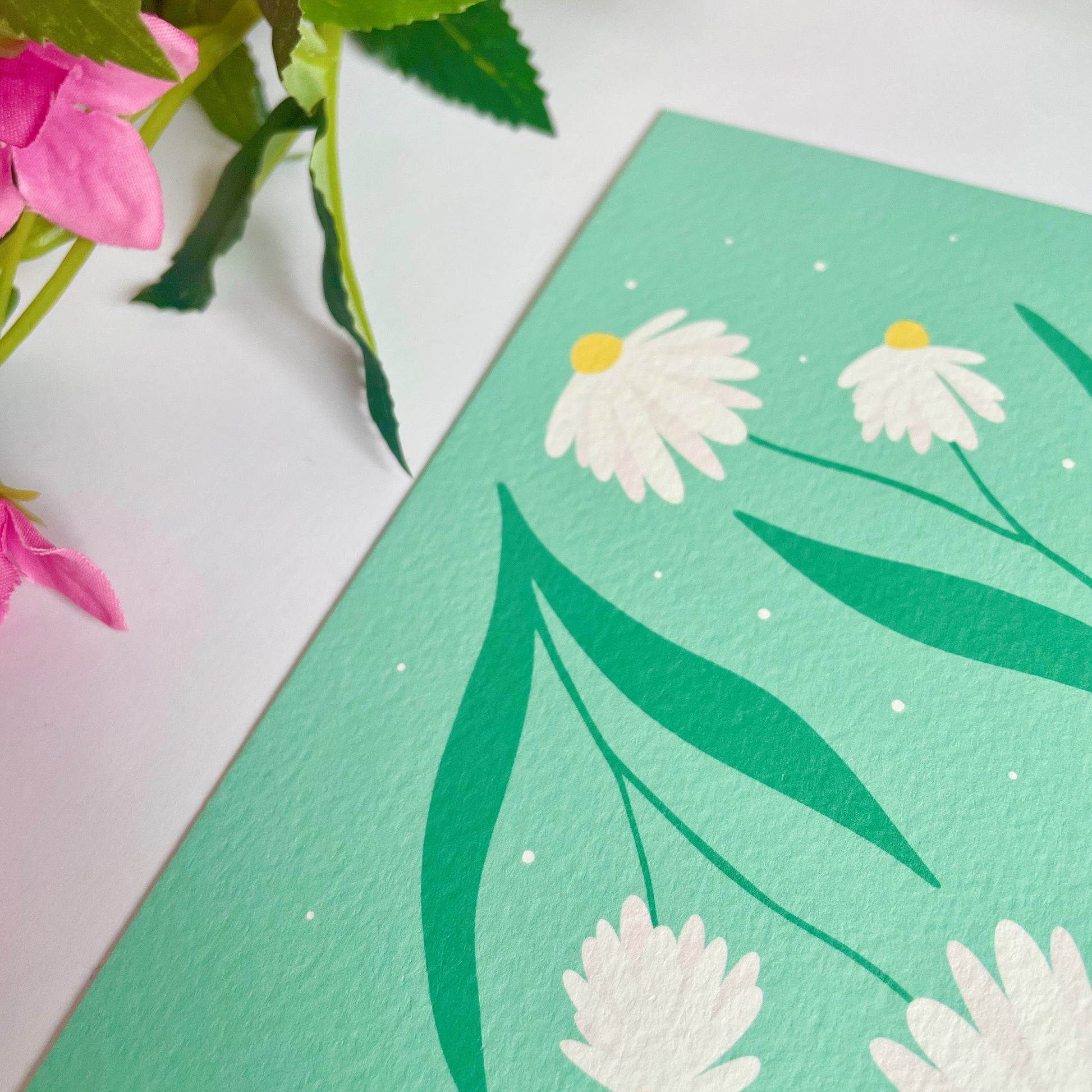 A textured postcard, with two illustrations of daisy stems on the front.