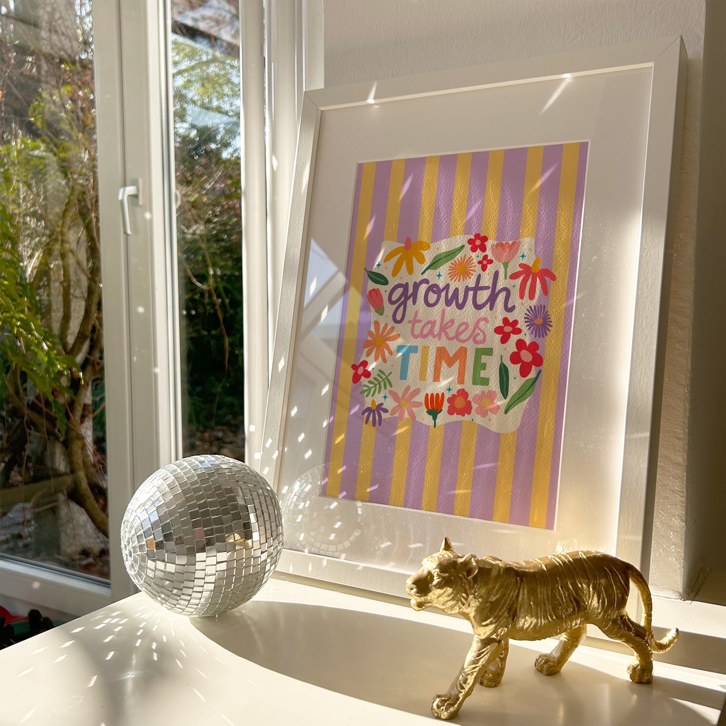 A lilac and yellow striped print, with a white wavy square in the centre that has floral illustrations and a positivity quote in the centre - that reads 'growth takes time'.
