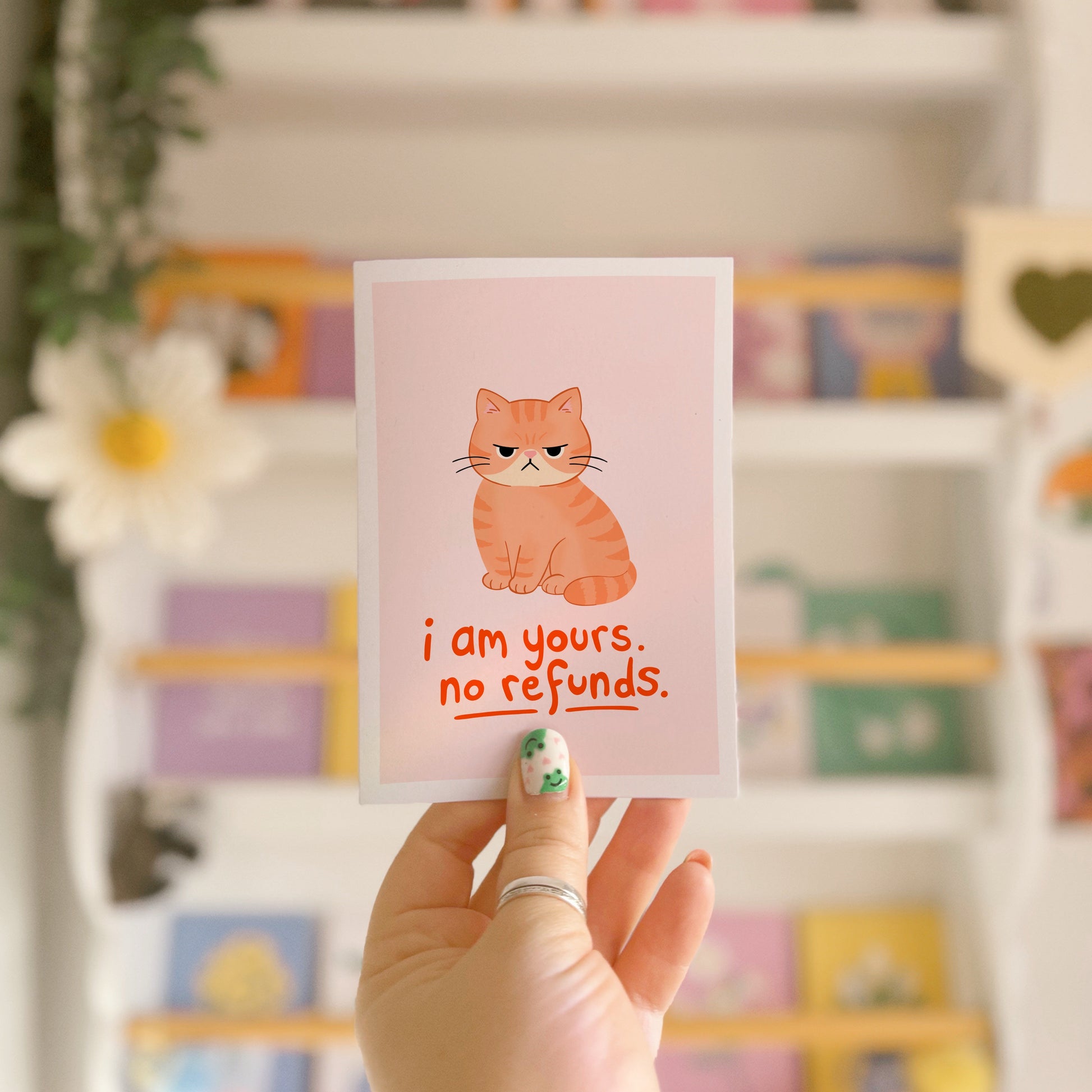 An illustrated card with a drawing of a grumpy orange cat, and words underneath that read 'I am yours, no refunds.'