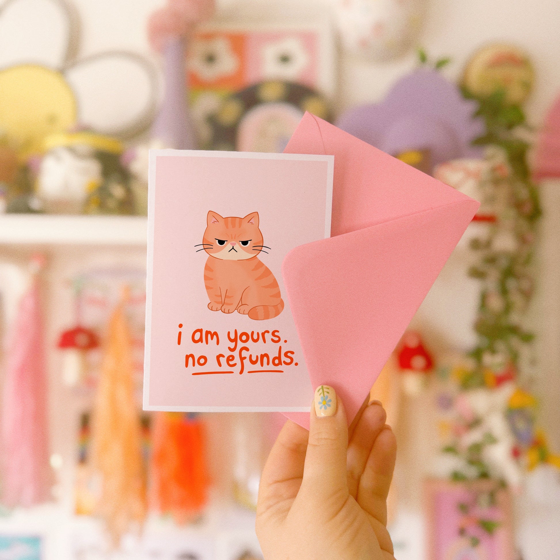 An illustrated card with a drawing of a grumpy orange cat, and words underneath that read 'I am yours, no refunds.'