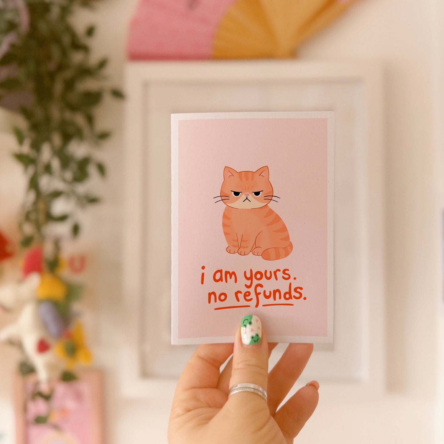 An illustrated card with a drawing of a grumpy orange cat, and words underneath that read 'I am yours, no refunds.'