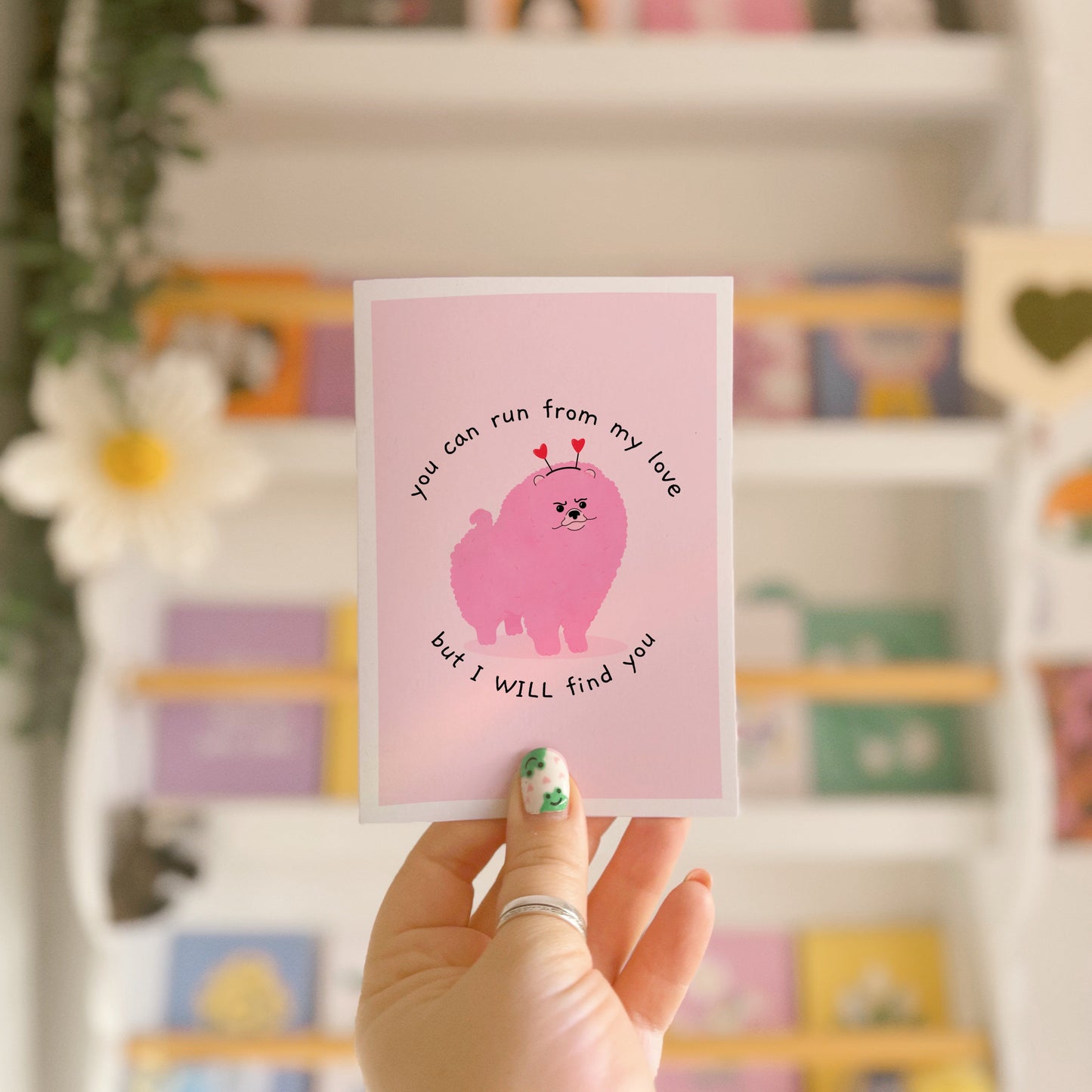A pink love themed card with an illustration of a pink grumpy dog on the front and text that reads 'you can run from my love, but I WILL find you'.