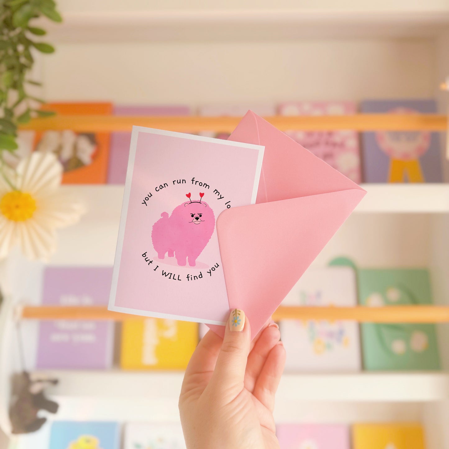 A pink love themed card with an illustration of a pink grumpy dog on the front and text that reads 'you can run from my love, but I WILL find you'.