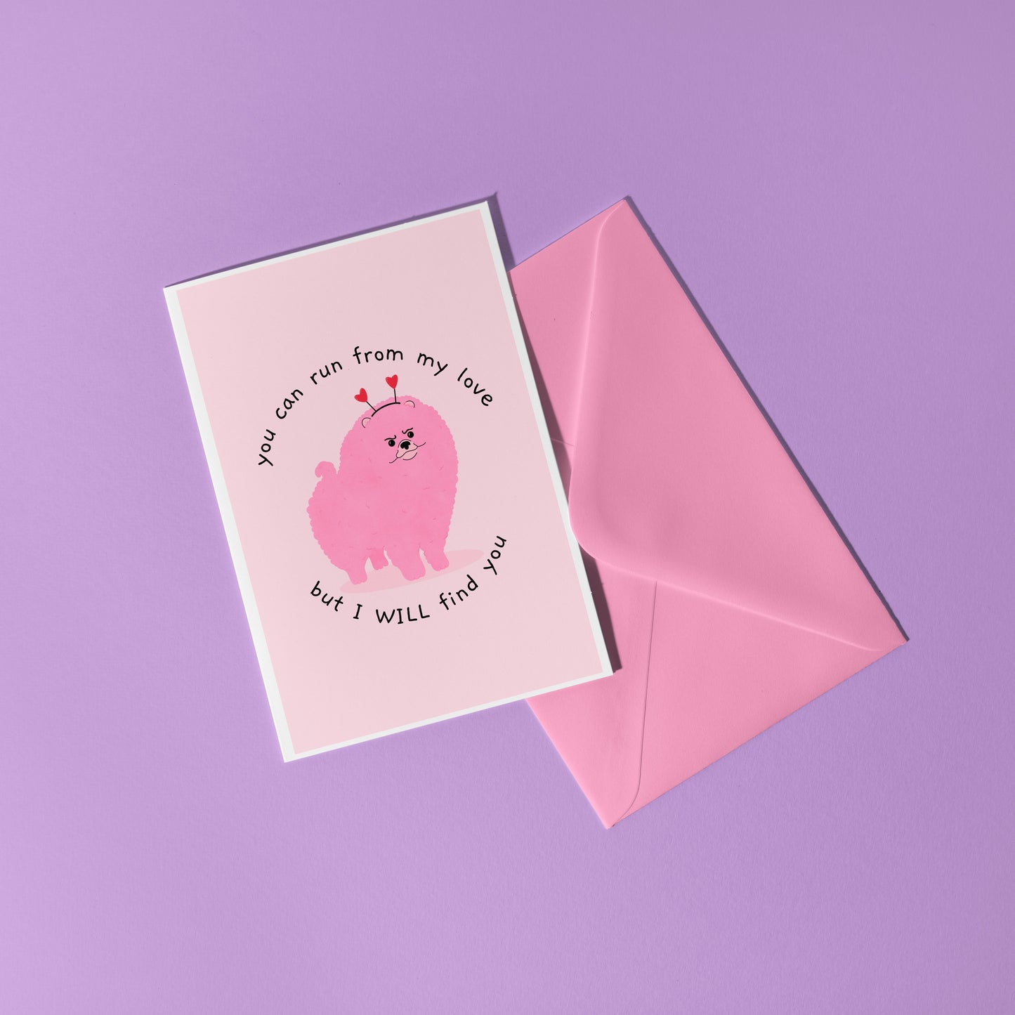 A pink love themed card with an illustration of a pink grumpy dog on the front and text that reads 'you can run from my love, but I WILL find you'.