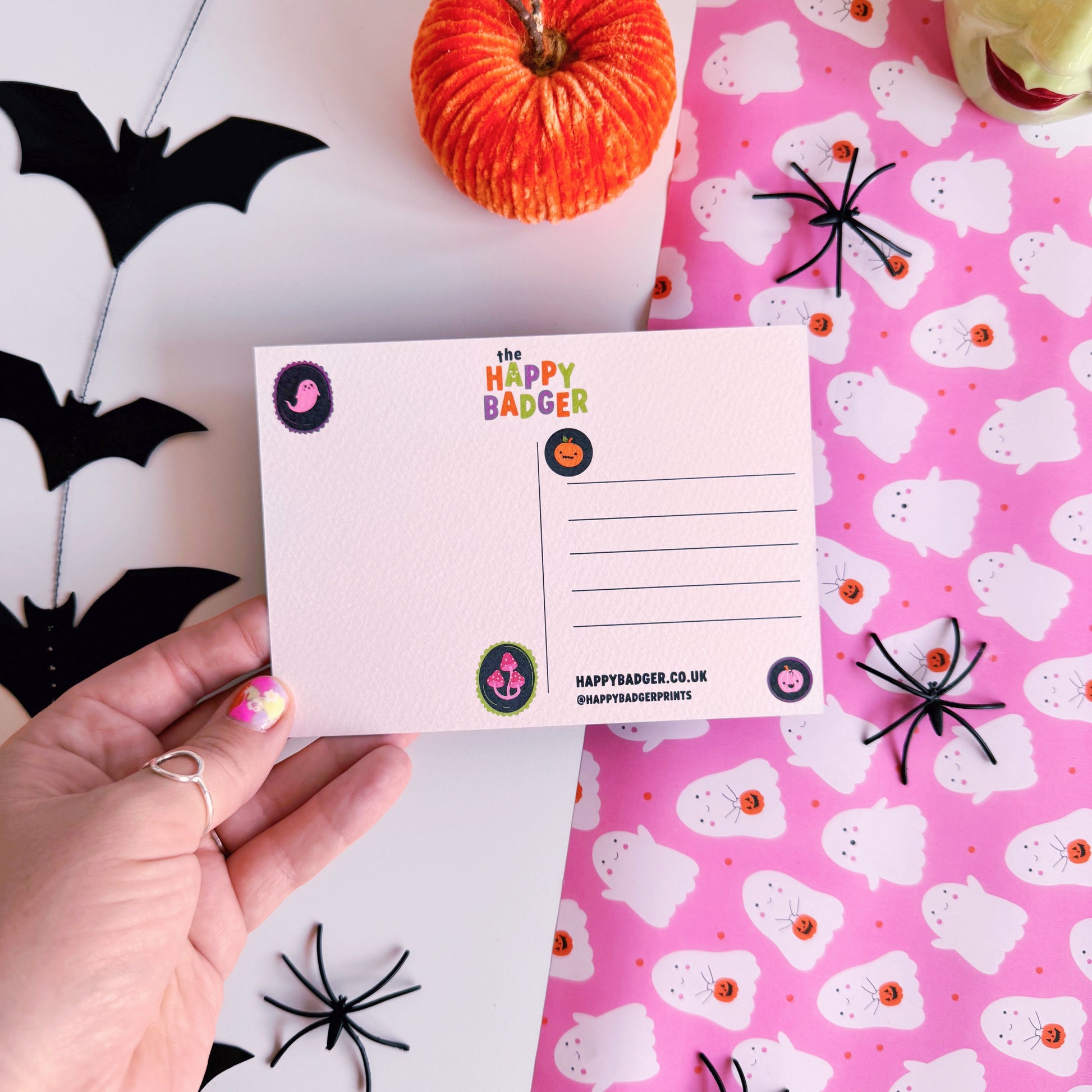 A halloween themed postcard of 5 ghosts hanging on a washing line, on a pink background.