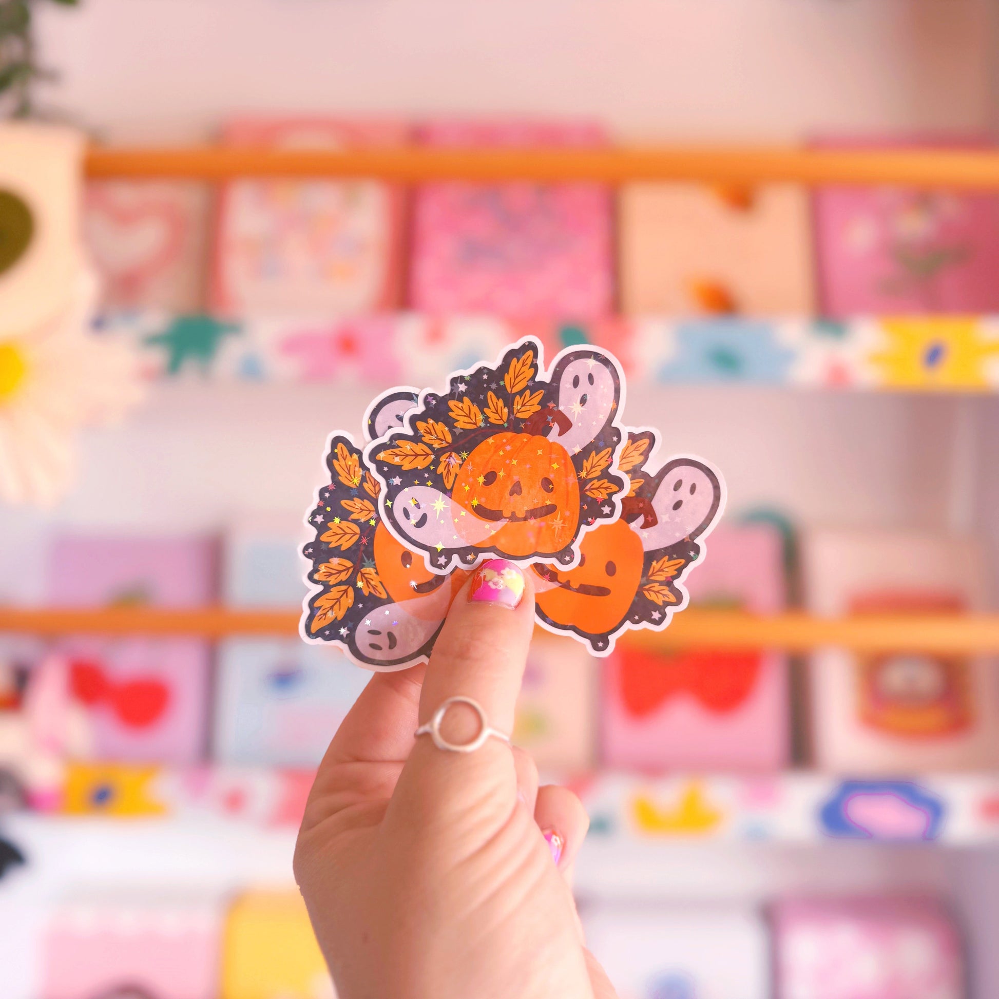 A holographic sticker with an illustration of a smiling pumpkin, with ghosts coming out of his mouth.