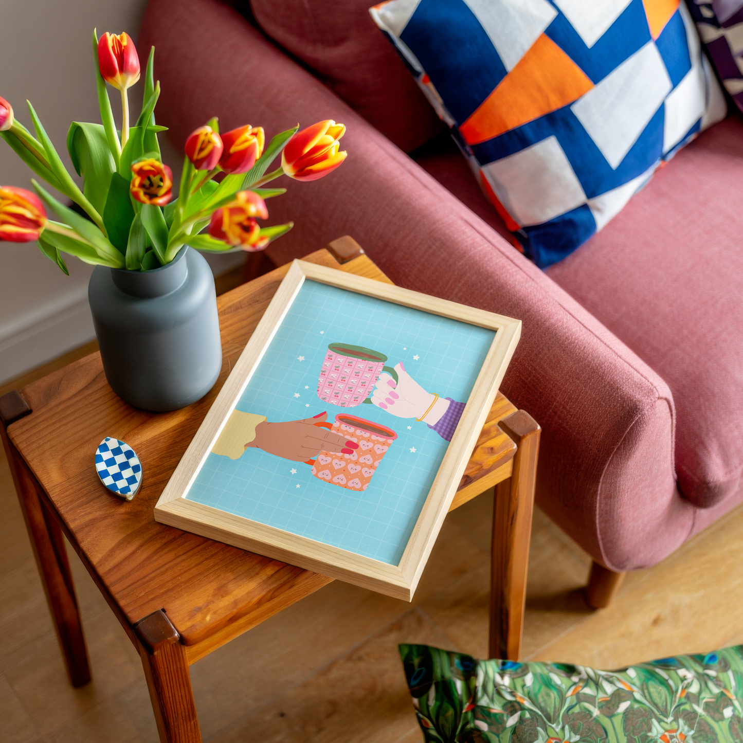 An illustrated print of two hands holding a colourful patterned mug each. The print has a blue background with little star illustrations.