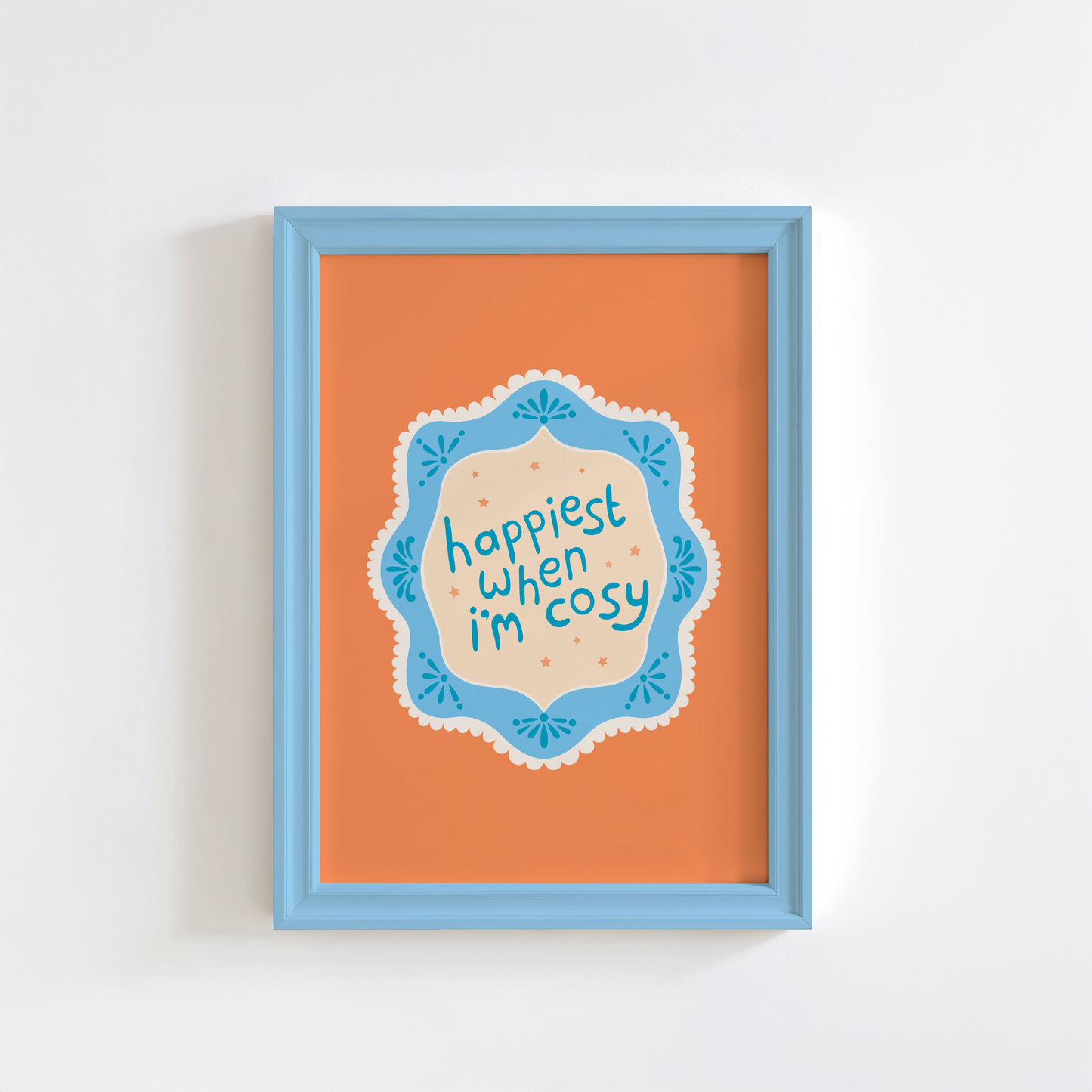 An orange print with a quote inside an illustrated blue decorative border - which says 'happiest when I'm cosy'.