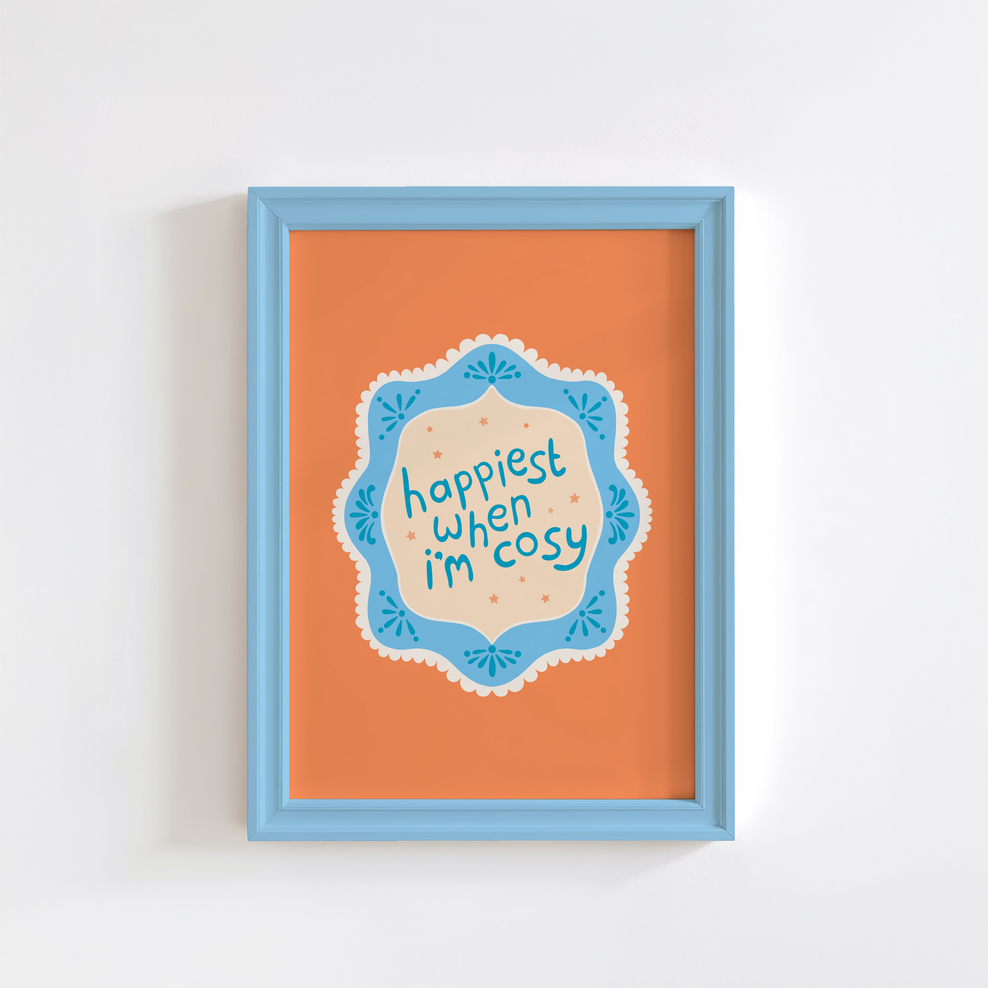 An orange print with a quote inside an illustrated blue decorative border - which says 'happiest when I'm cosy'.