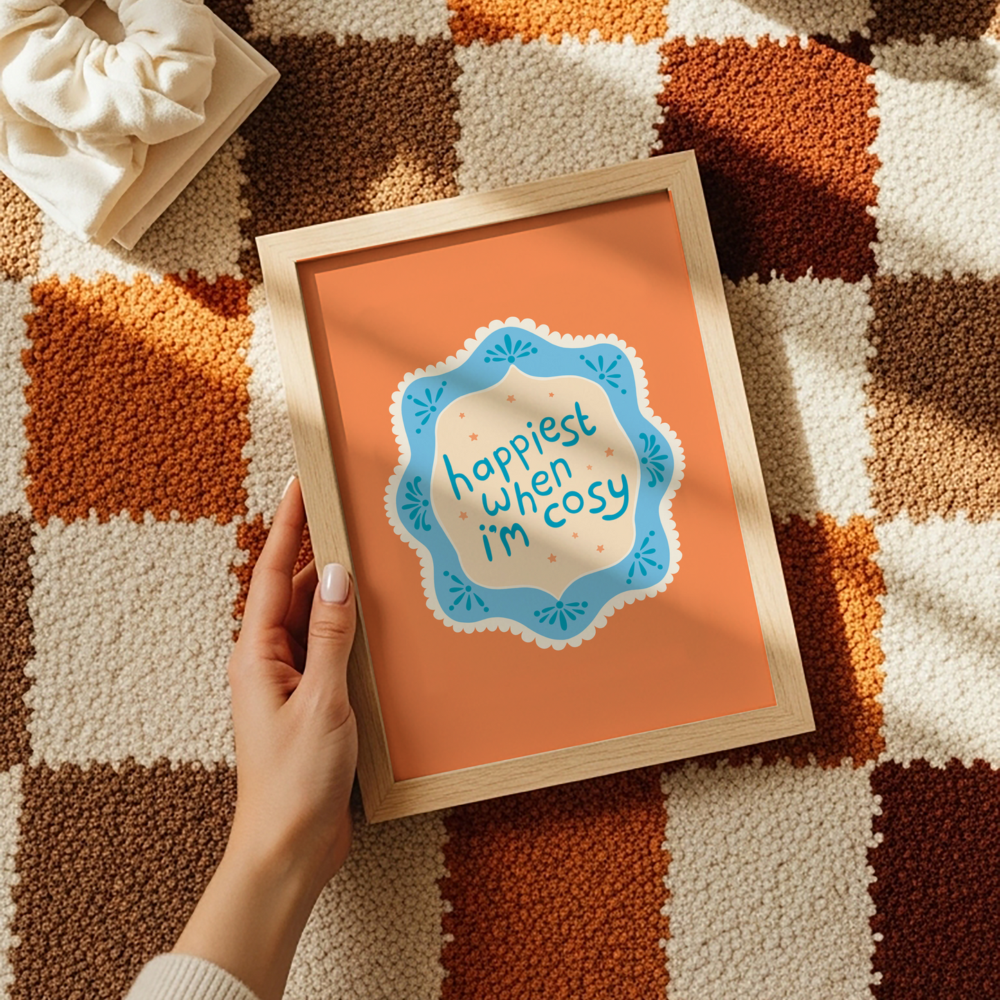 An orange print with a quote inside an illustrated blue decorative border - which says 'happiest when I'm cosy'.