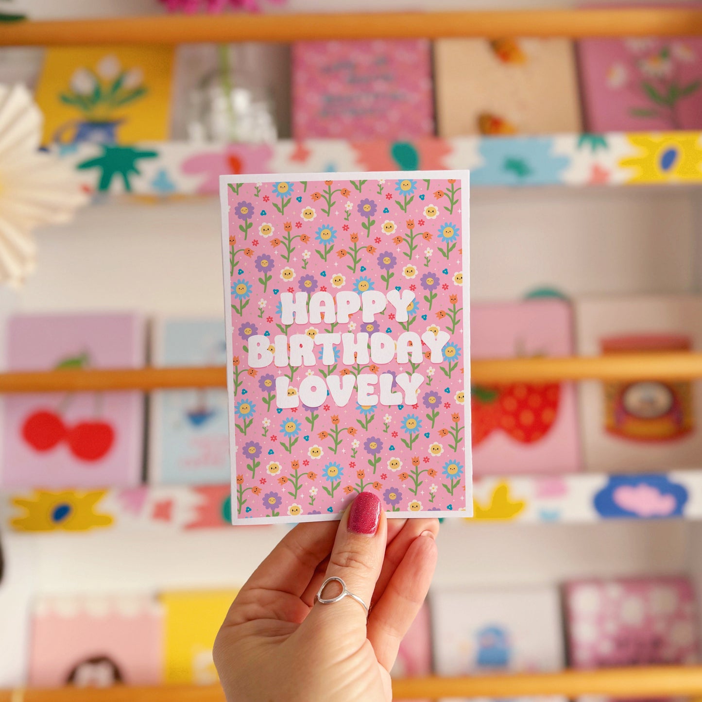 A pink floral birthday card, with white text that reads 'Happy Birthday Lovely'.
