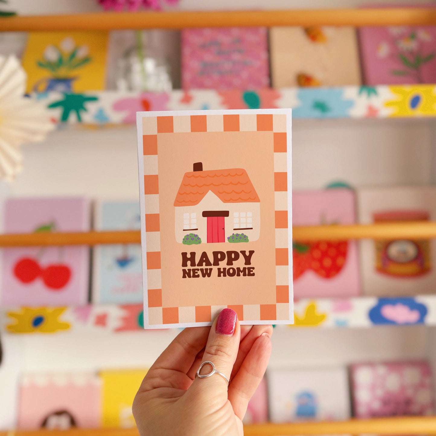 An orange card, with an illustration of a cute cottage on the front and the words 'happy new home' underneath.