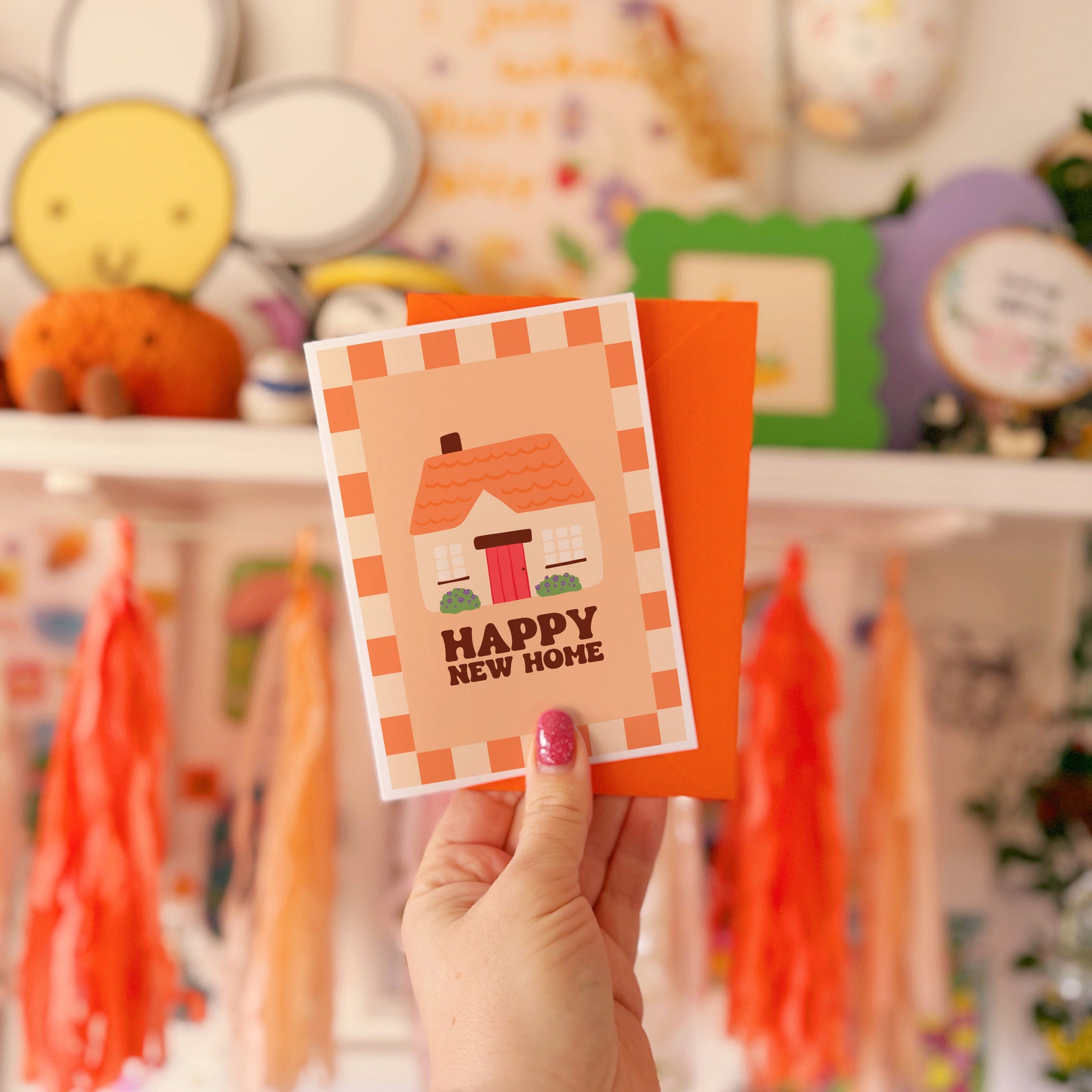 An orange card, with an illustration of a cute cottage on the front and the words 'happy new home' underneath.