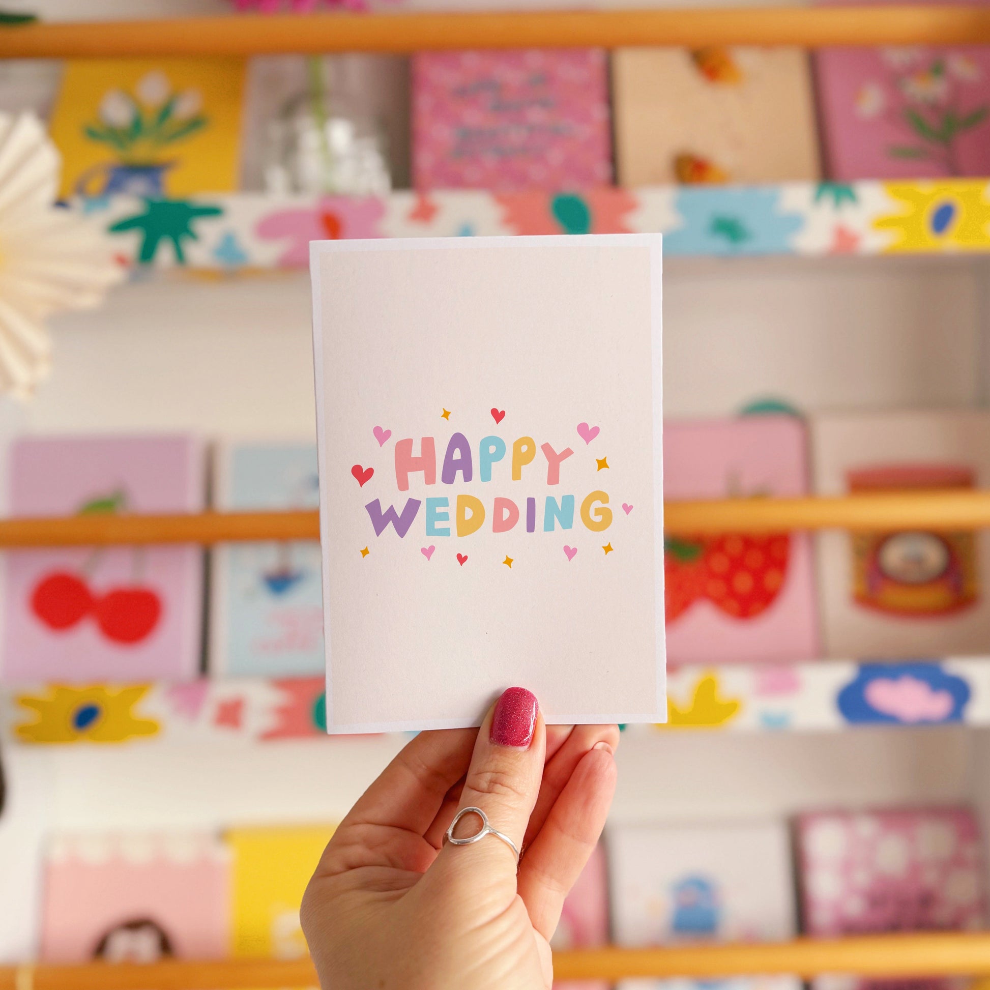A minimalistic card with colourful hand lettering that reads 'Happy Wedding' with little heart and star doodles around it.