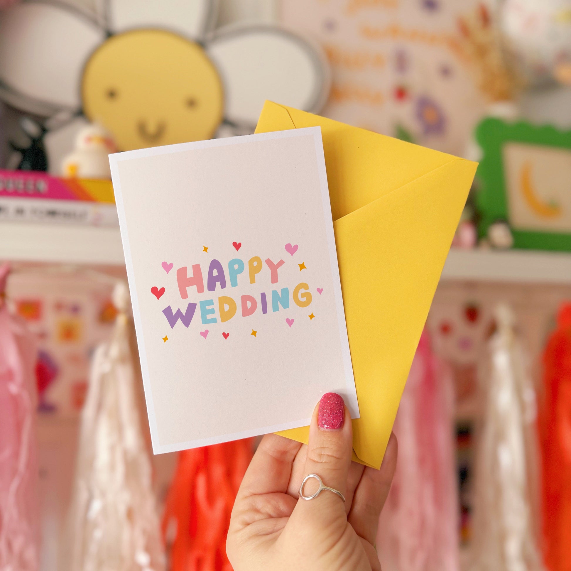 A minimalistic card with colourful hand lettering that reads 'Happy Wedding' with little heart and star doodles around it.