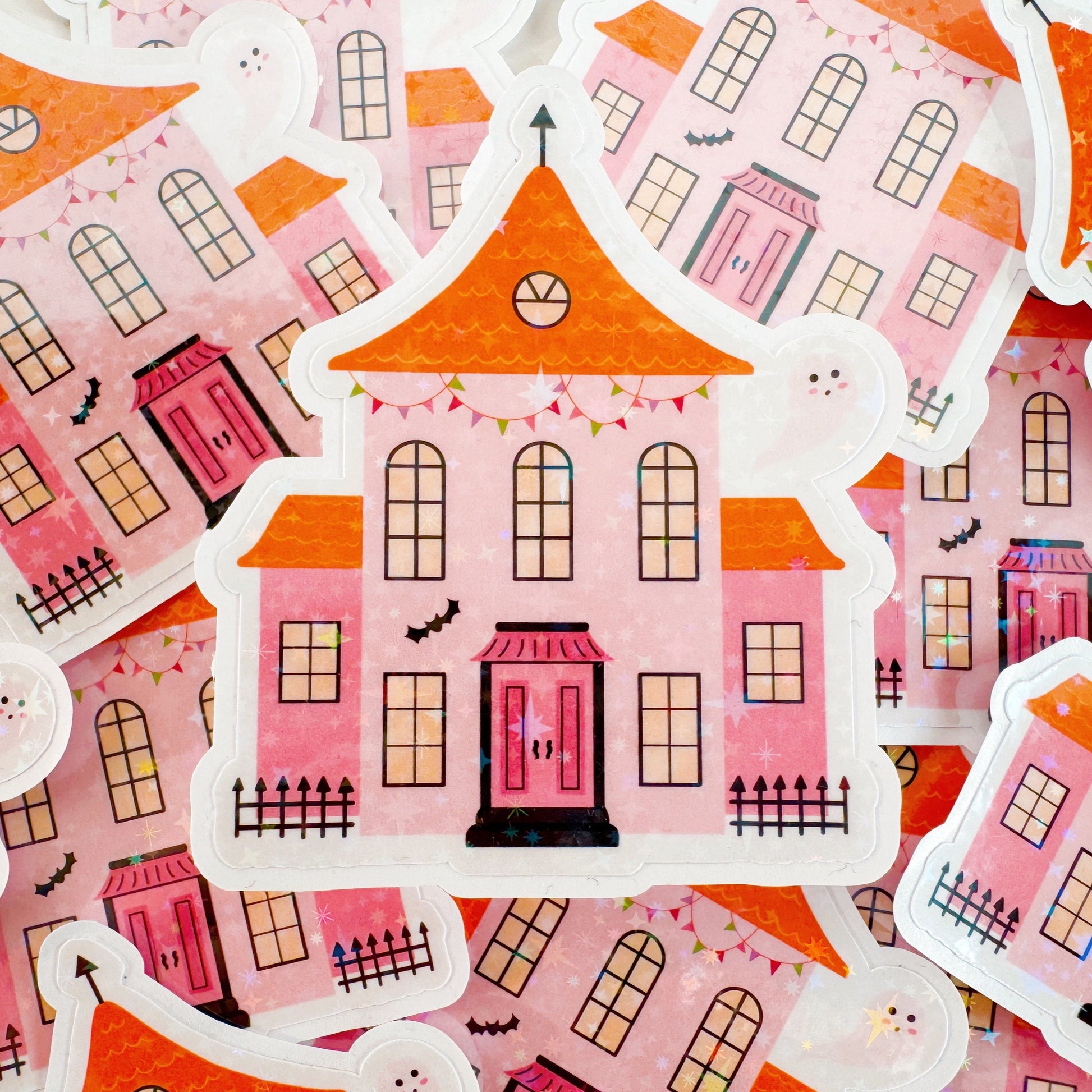 A holographic sticker, a pink and orange haunted house with a glittery finish. The sticker has an easy peel lip.