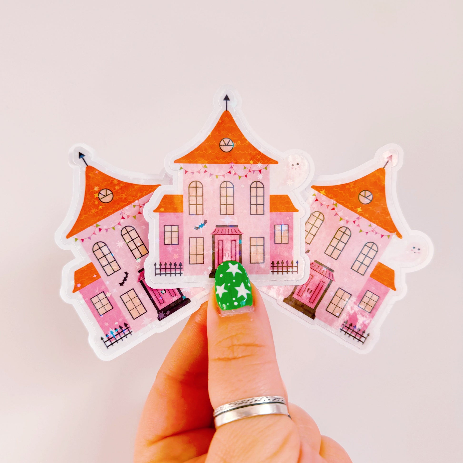 A holographic sticker, a pink and orange haunted house with a glittery finish. The sticker has an easy peel lip.