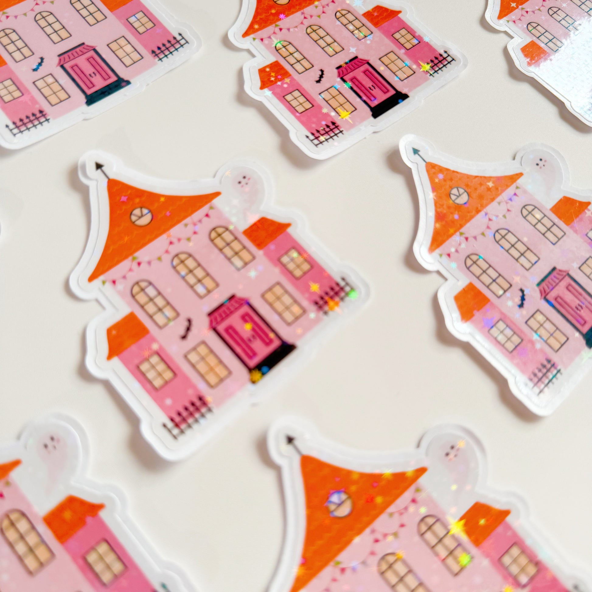 A holographic sticker, a pink and orange haunted house with a glittery finish. The sticker has an easy peel lip.