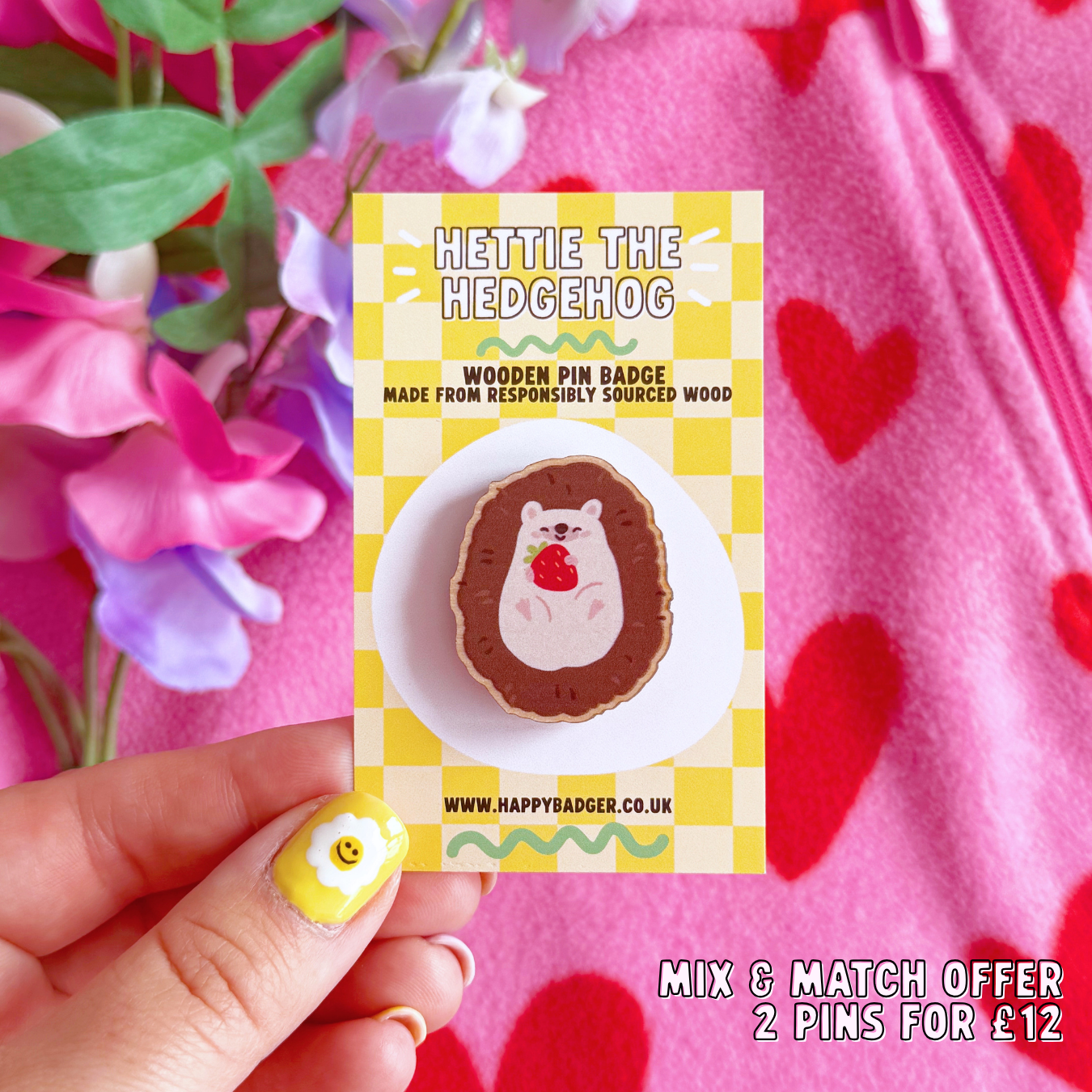 A wooden pin badge featuring a cute hedgehog curled up in a ball, with a little smiling face, holding a red strawberry in her arms.