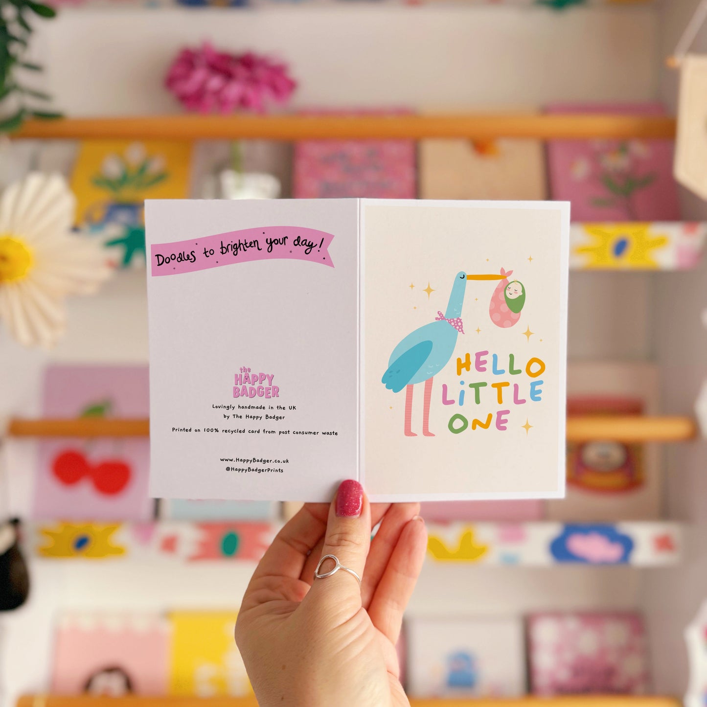 A greetings card with an illustration of a stalk carrying a baby, with the words 'hello little one' in colourful tones.