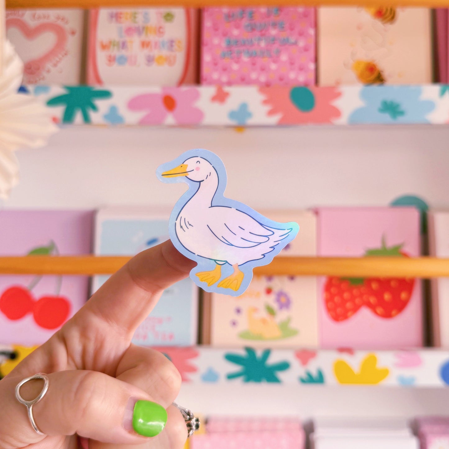 A sticker with an illustration of a white goose, smiling. The sticker has a blue border and the backing has an easy peel lip.