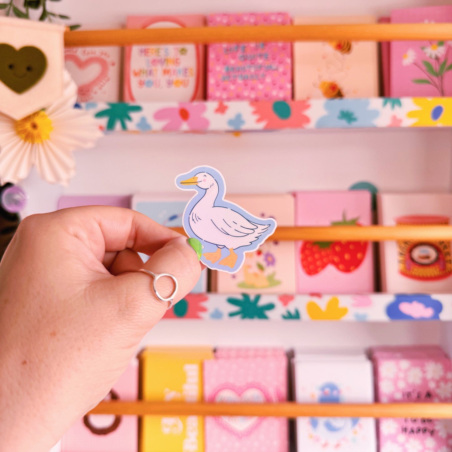 A sticker with an illustration of a white goose, smiling. The sticker has a blue border and the backing has an easy peel lip.