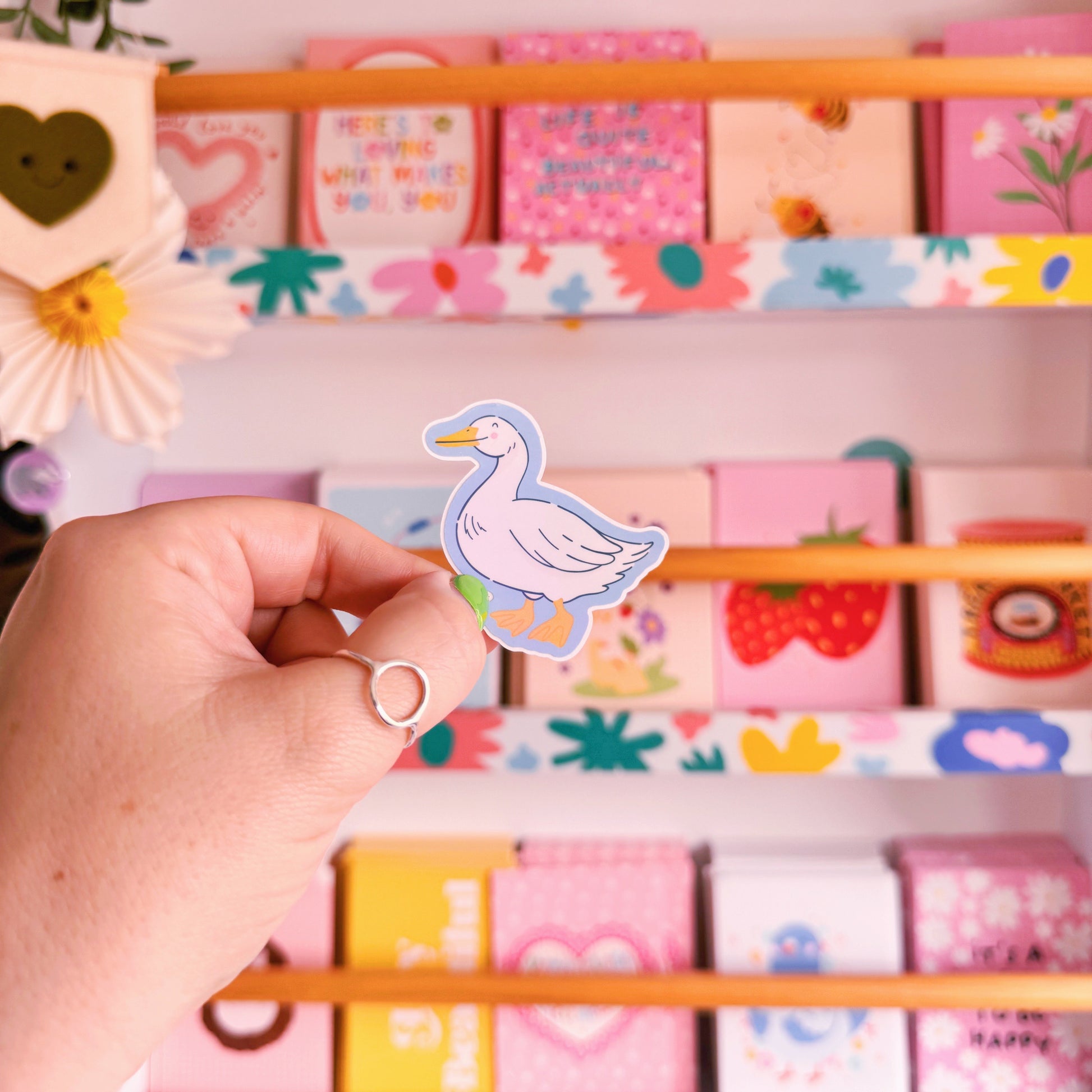 A sticker with an illustration of a white goose, smiling. The sticker has a blue border and the backing has an easy peel lip.