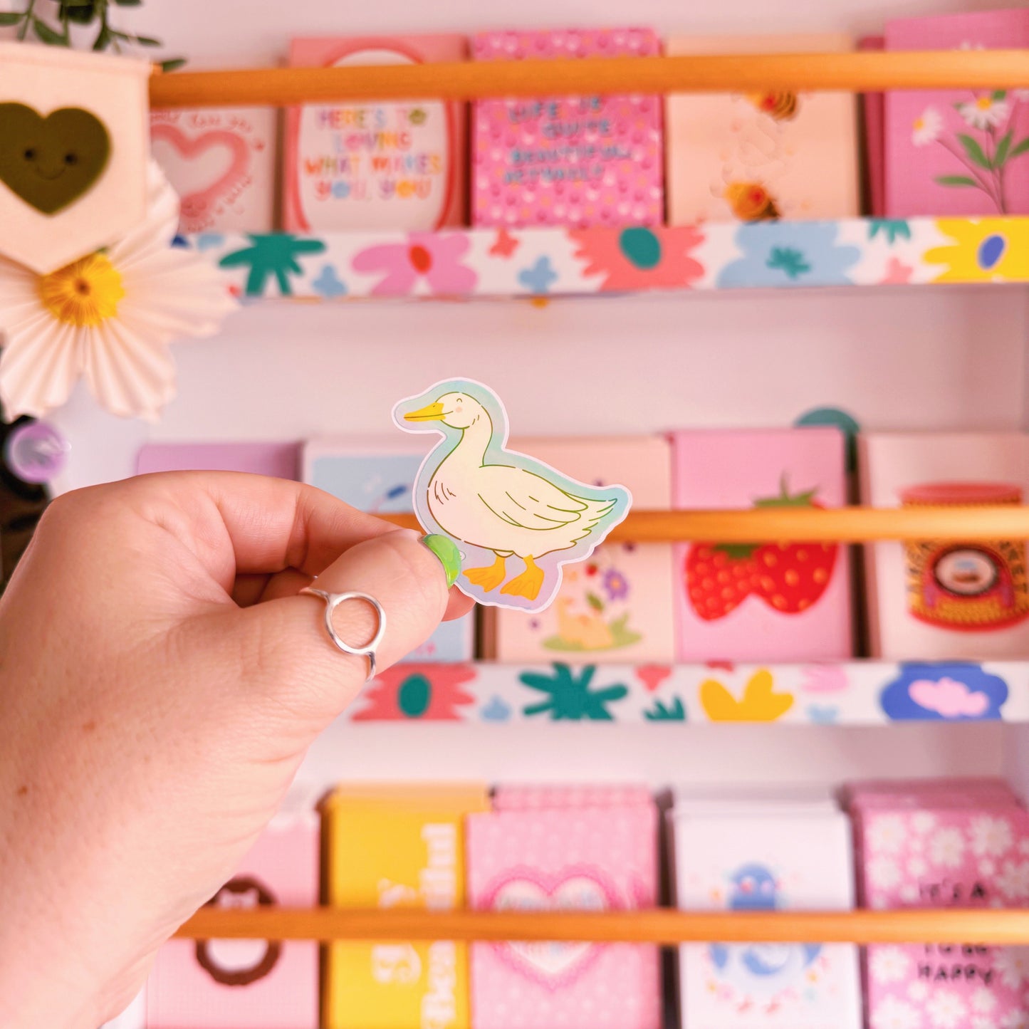 A sticker with an illustration of a white goose, smiling. The sticker has a blue border and the backing has an easy peel lip.