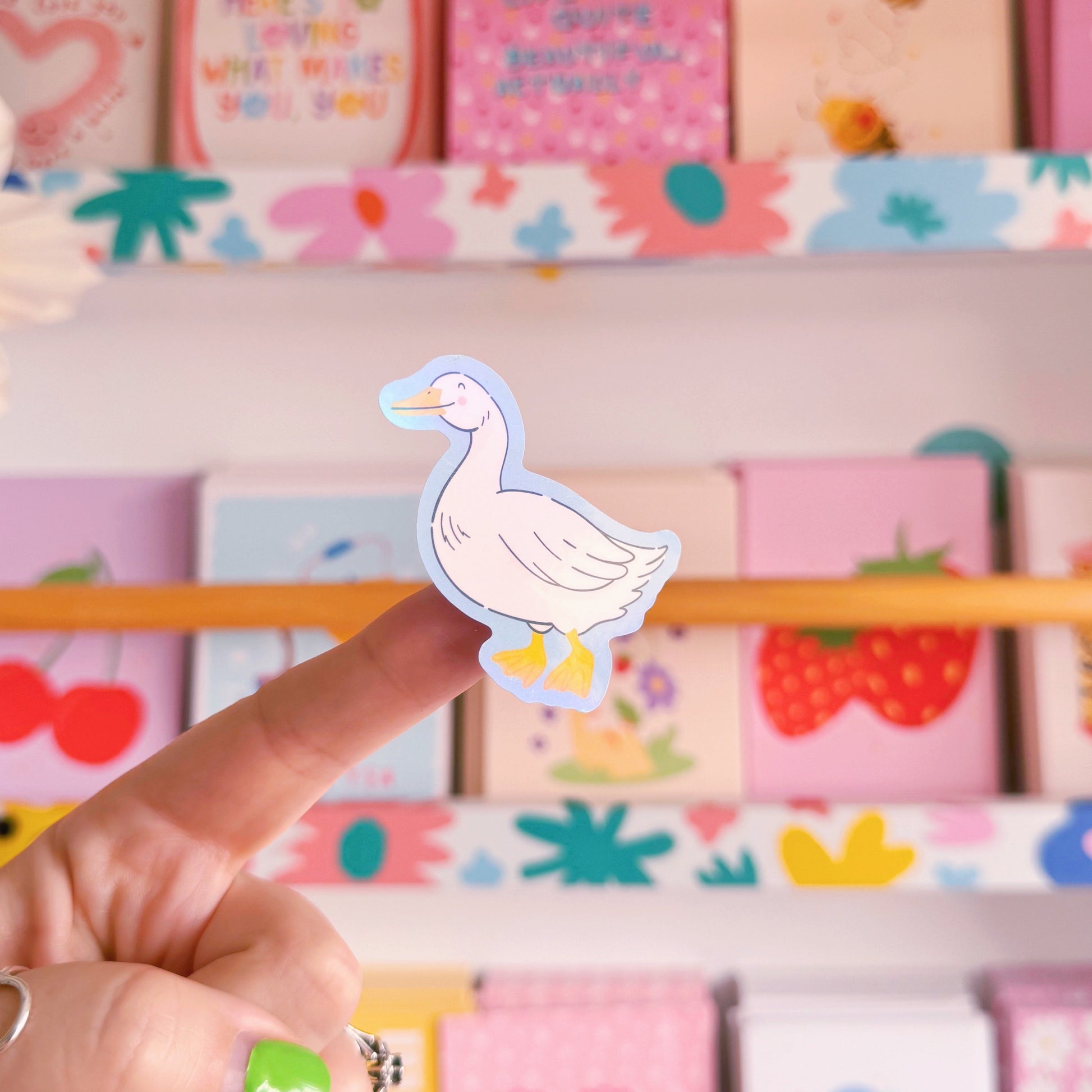 A sticker with an illustration of a white goose, smiling. The sticker has a blue border and the backing has an easy peel lip.